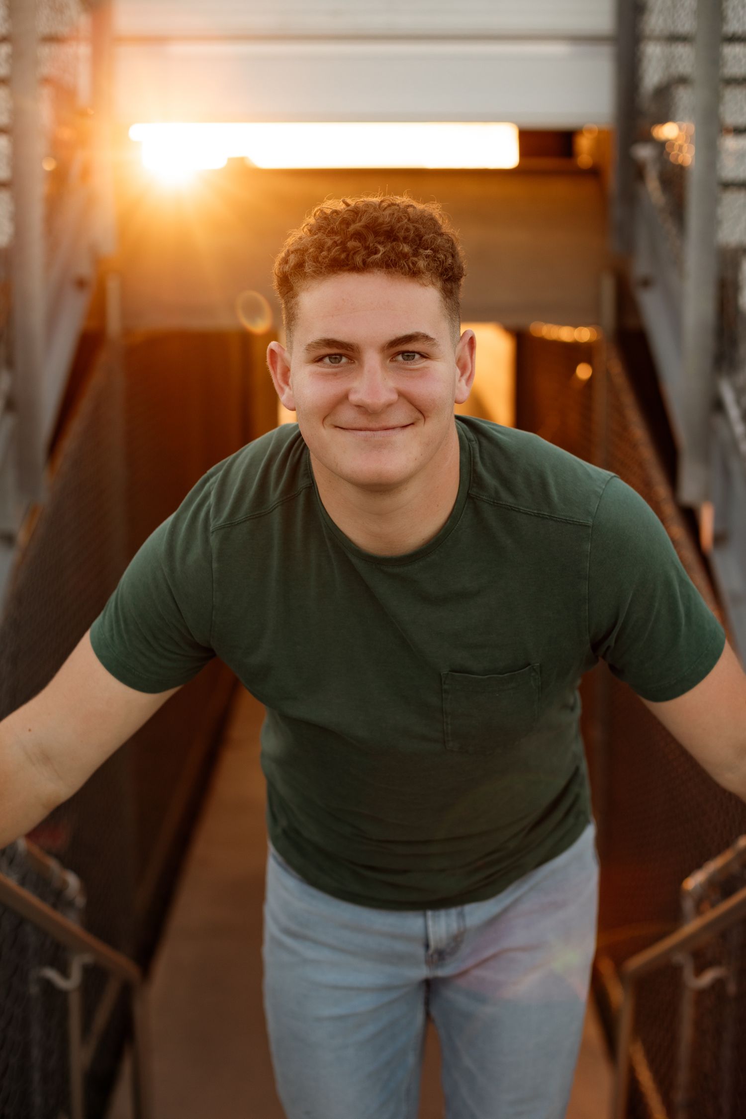 Smiling young man in a green t-shirt and jeans standing on a bridge at golden hour.