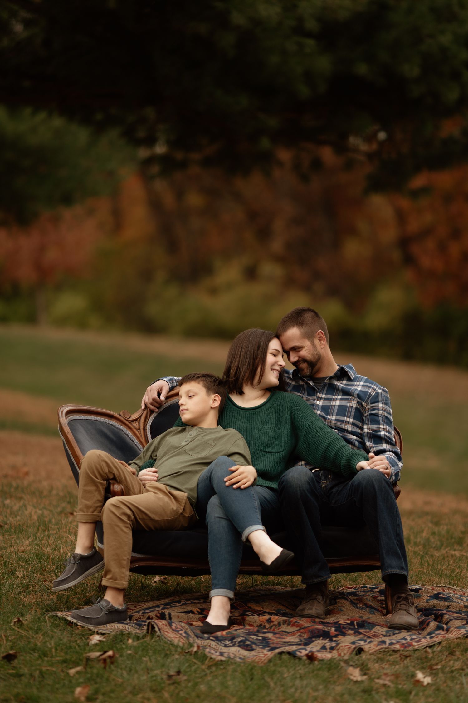 Family of three sitting together on a vintage sofa outdoors in a fall park setting.
