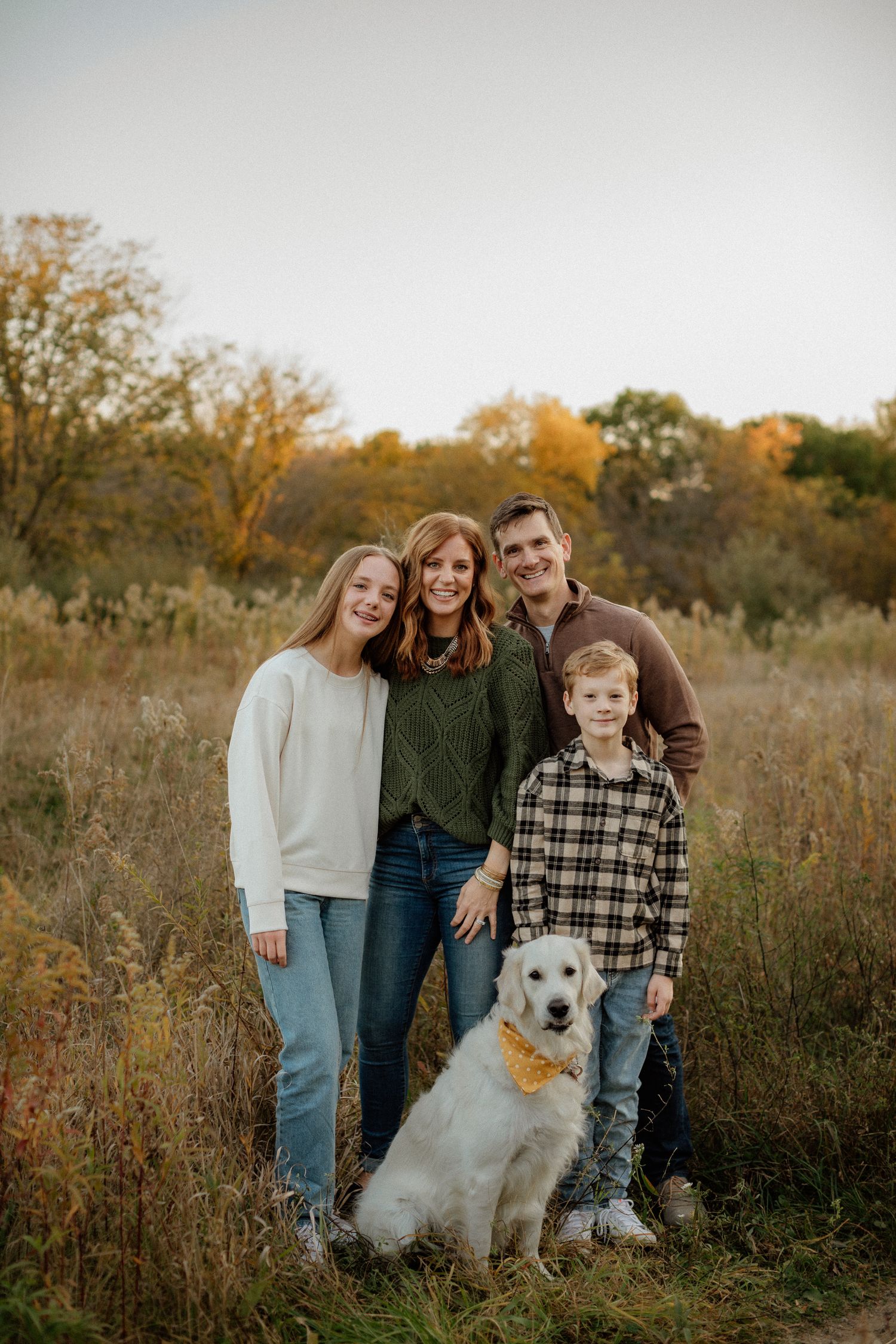 A family of four poses with their golden retriever in a sunlit autumn meadow.