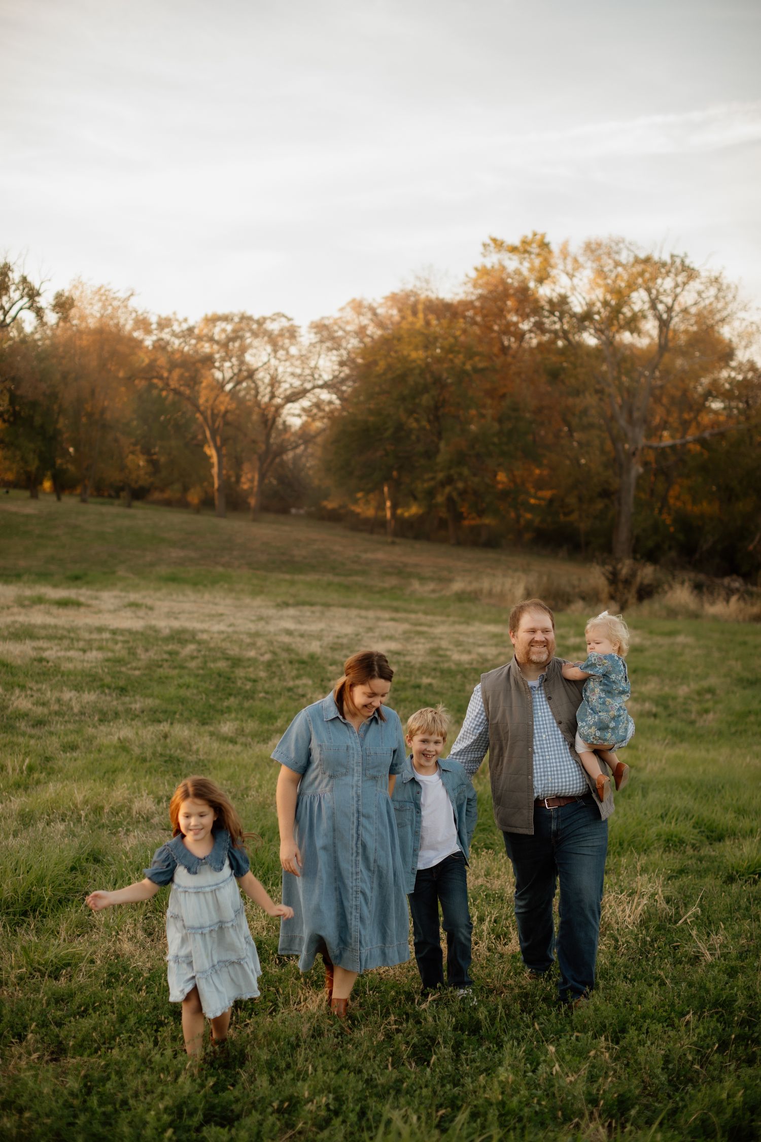 Happy family of five walking through a green meadow during golden hour sunset.