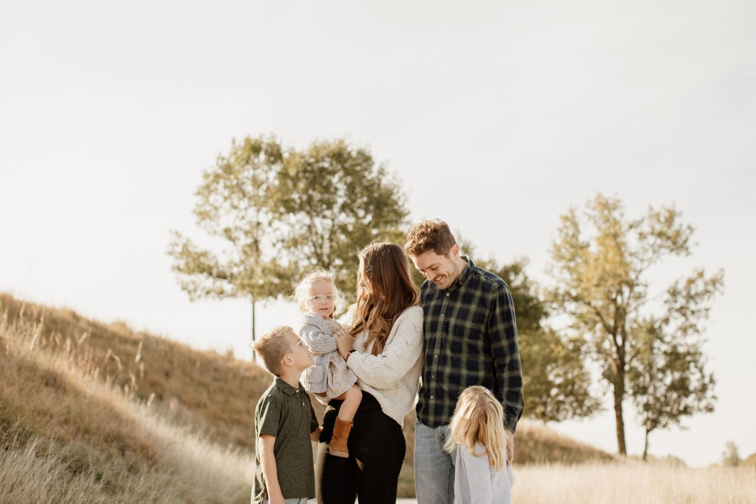 Happy family of five enjoying a sunny day together in a golden meadow outdoors.