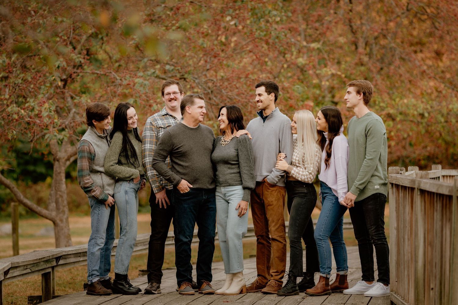 Large family group laughing together on a wooden bridge surrounded by colorful autumn foliage.