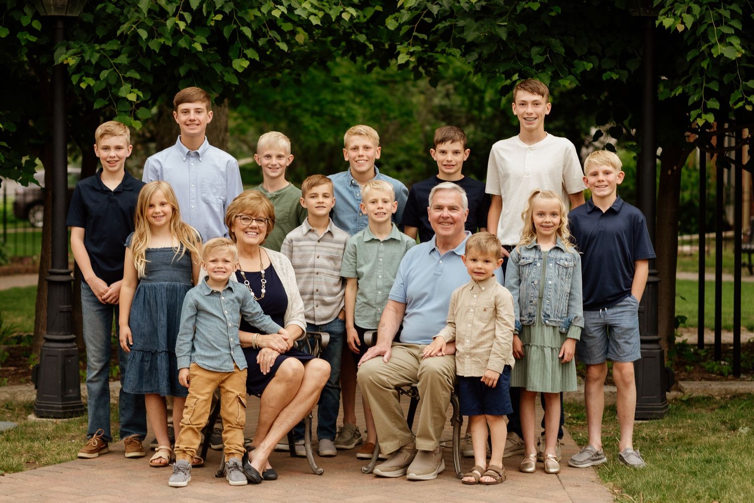 Large multigenerational family portrait with grandparents and grandchildren posing outdoors in a park setting.