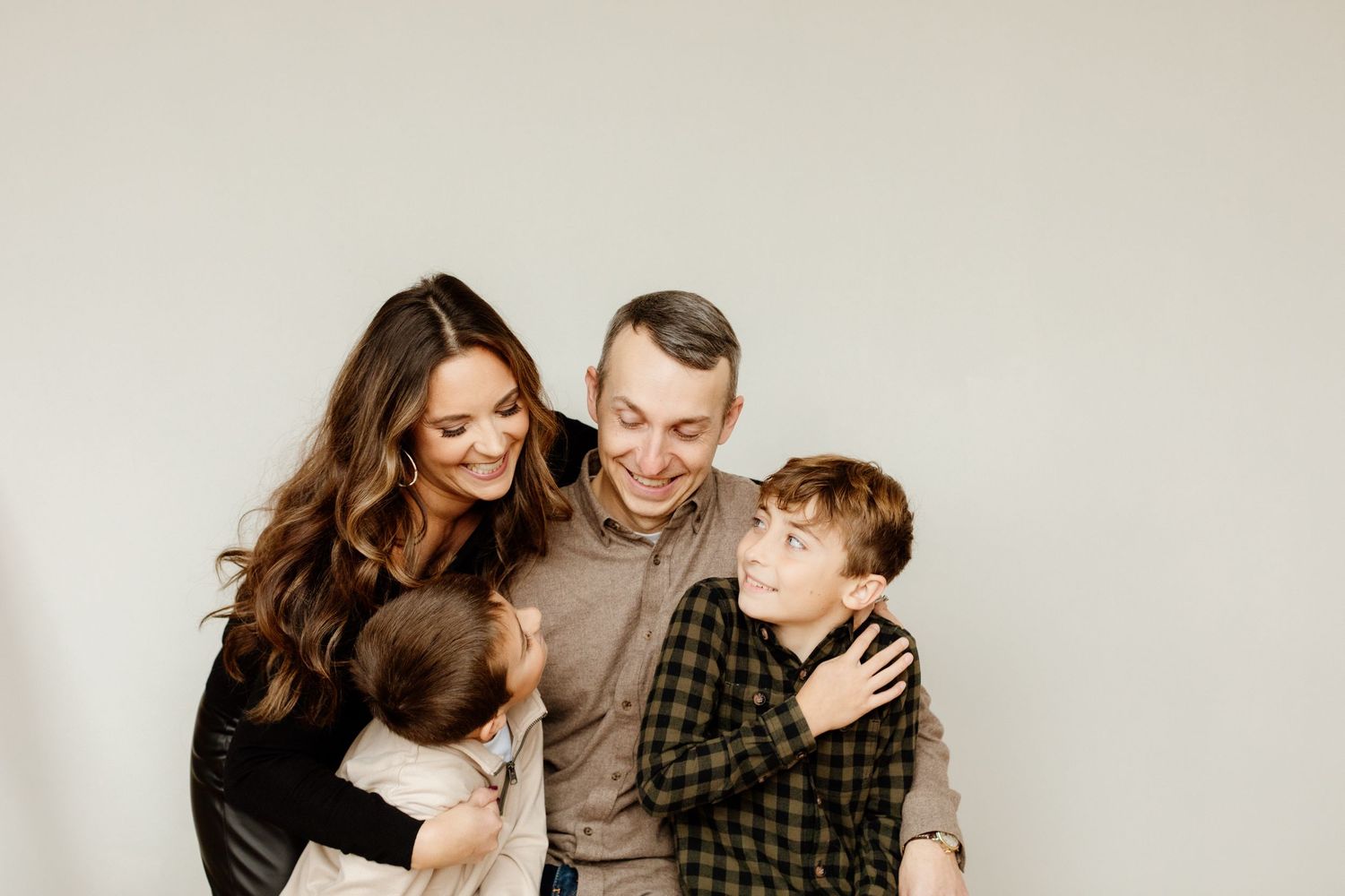 Smiling family of four posing together against a light gray studio background.