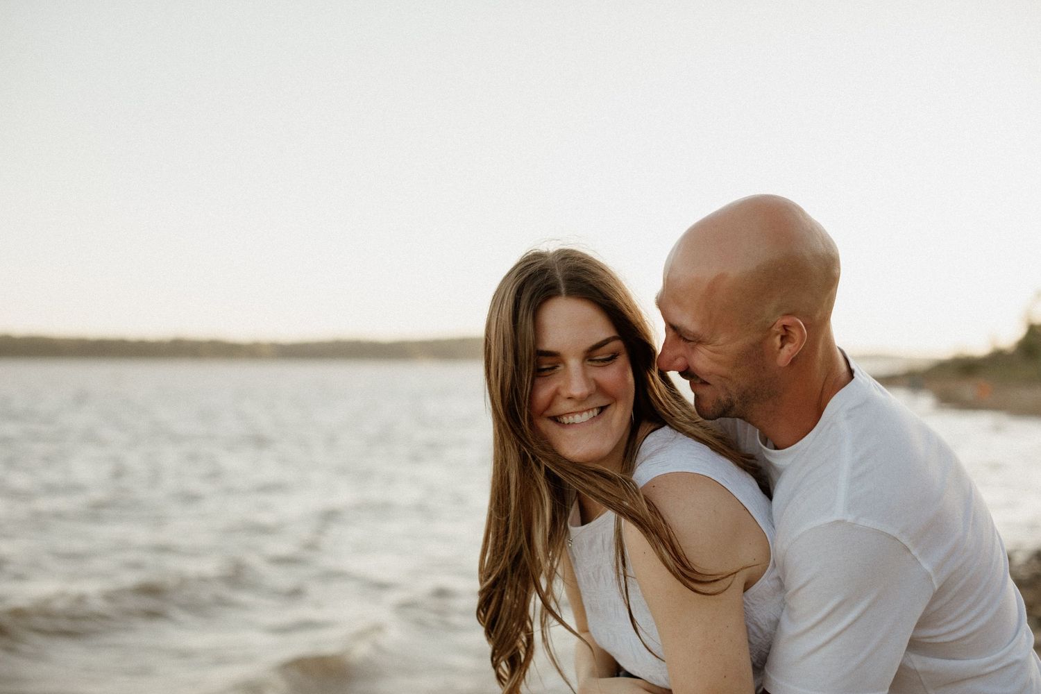Happy couple embracing and laughing together on a sandy beach at golden hour.