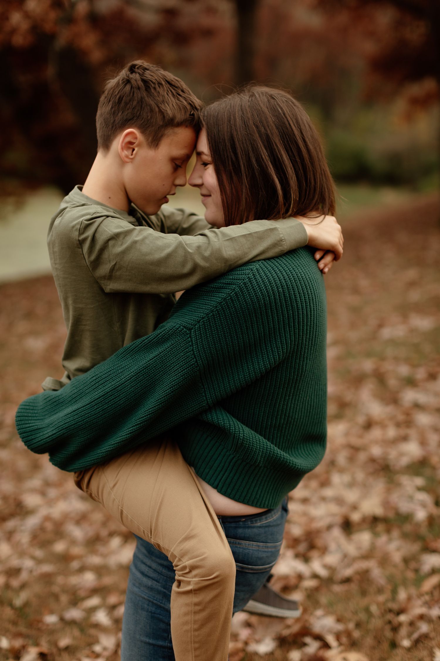 Mother and young son sharing a tender hug outdoors among autumn fallen leaves.