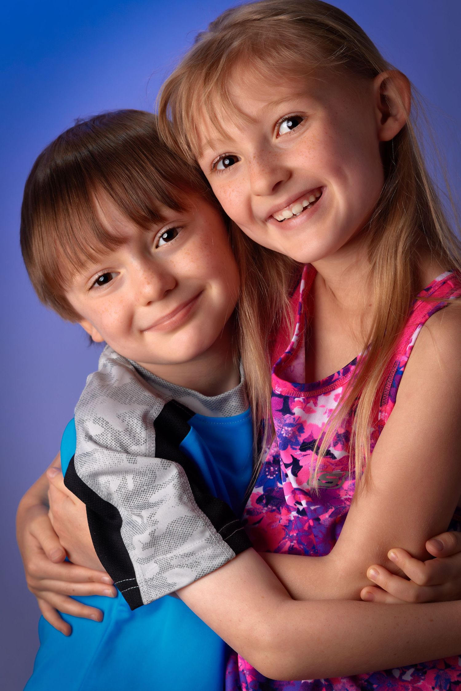 Two smiling children hugging each other in a studio portrait with blue background.