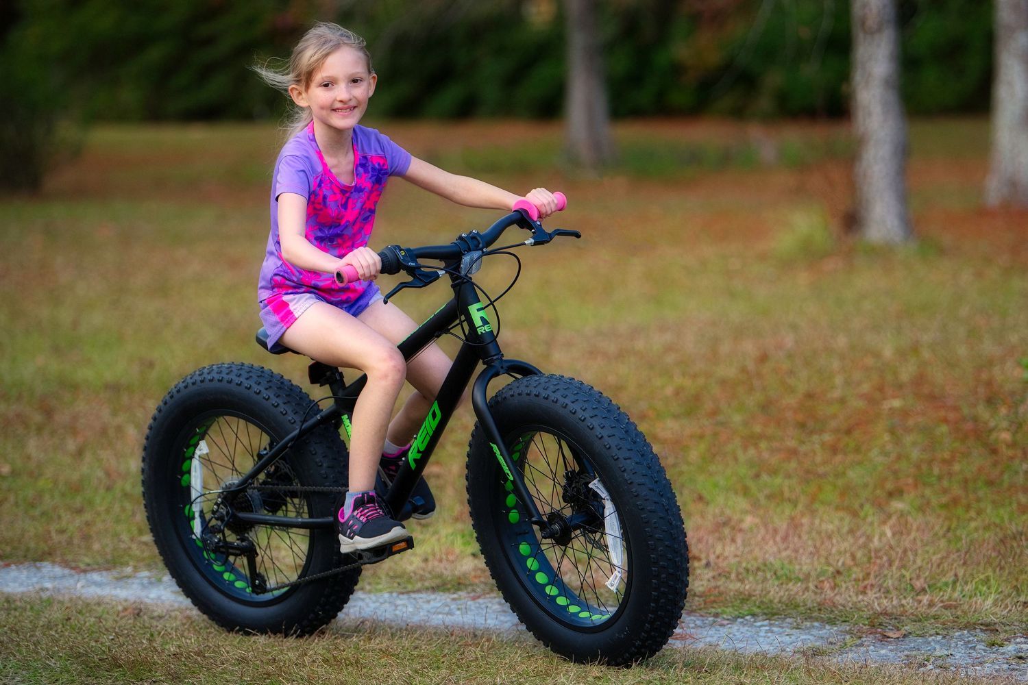 Young girl smiling while riding a black and green fat tire mountain bike outdoors.