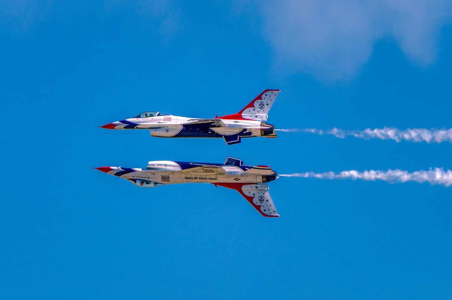 Two US Air Force Thunderbirds jets flying in close formation with white smoke trails.