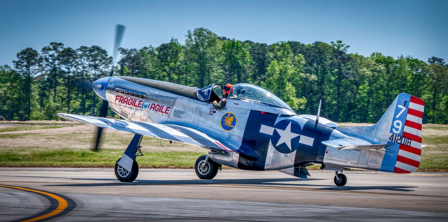 Restored P-51 Mustang WWII fighter plane taxiing on runway with American flag markings.