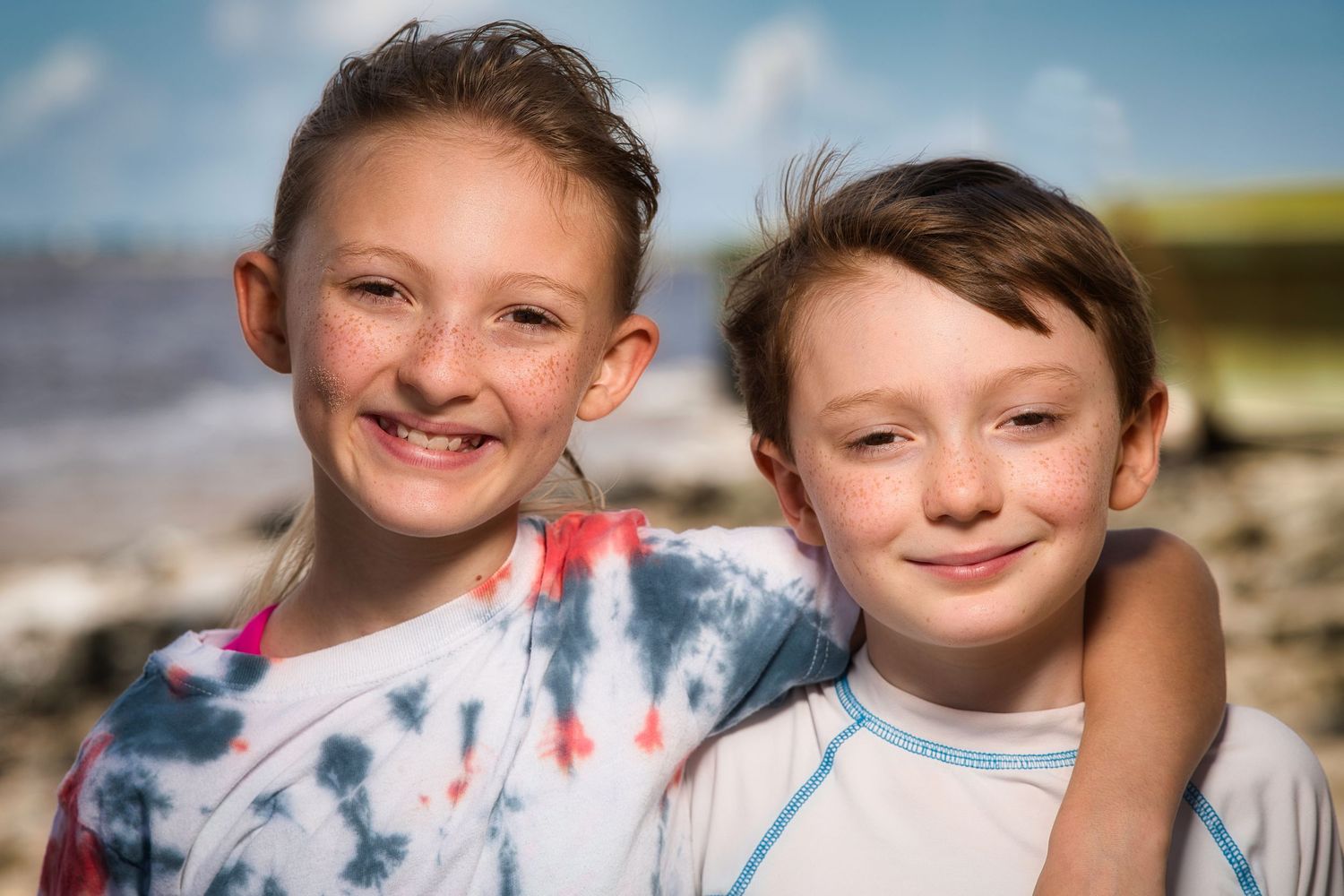 Two smiling children hugging on a sunny beach.