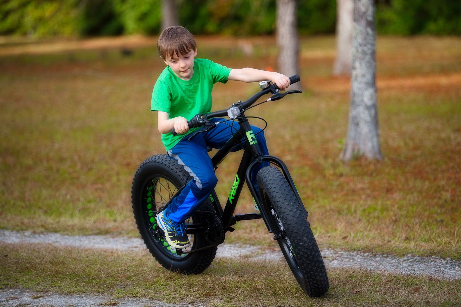 Young boy riding a fat tire bike on a gravel path in a park.