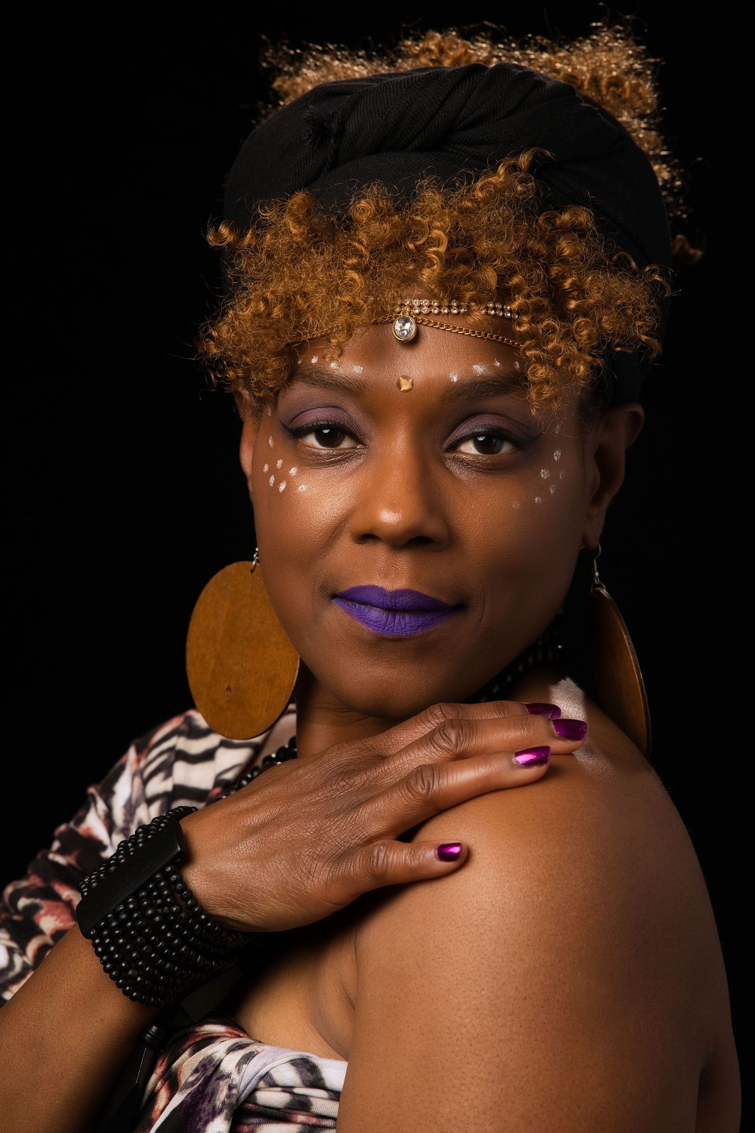 African woman with tribal face paint, purple lips, and curly hair posing.