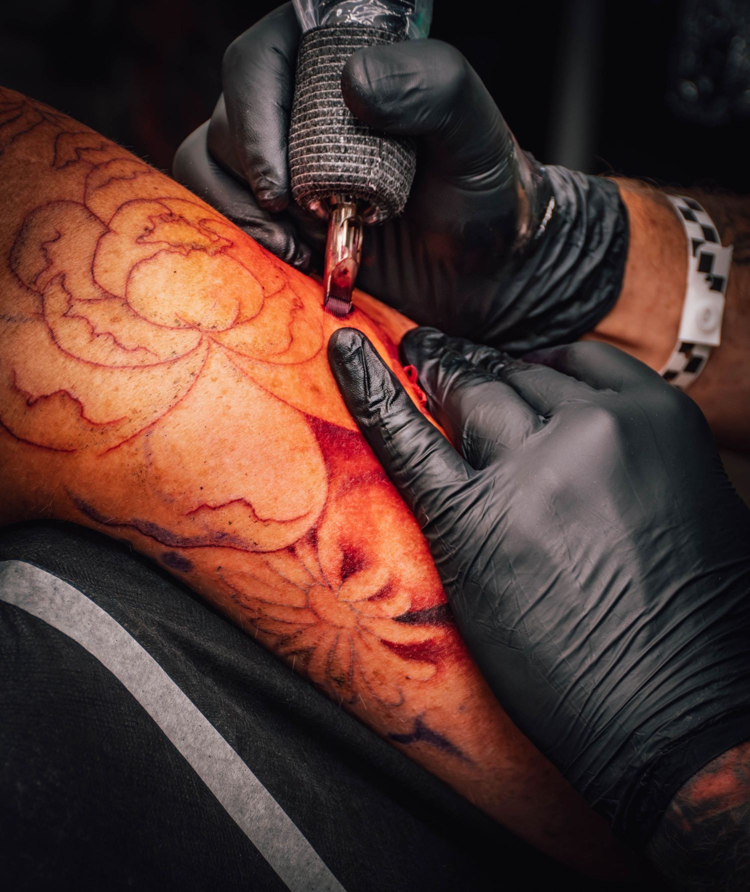 Tattoo artist in black gloves using a tattoo machine to ink a floral design on a client's arm.
