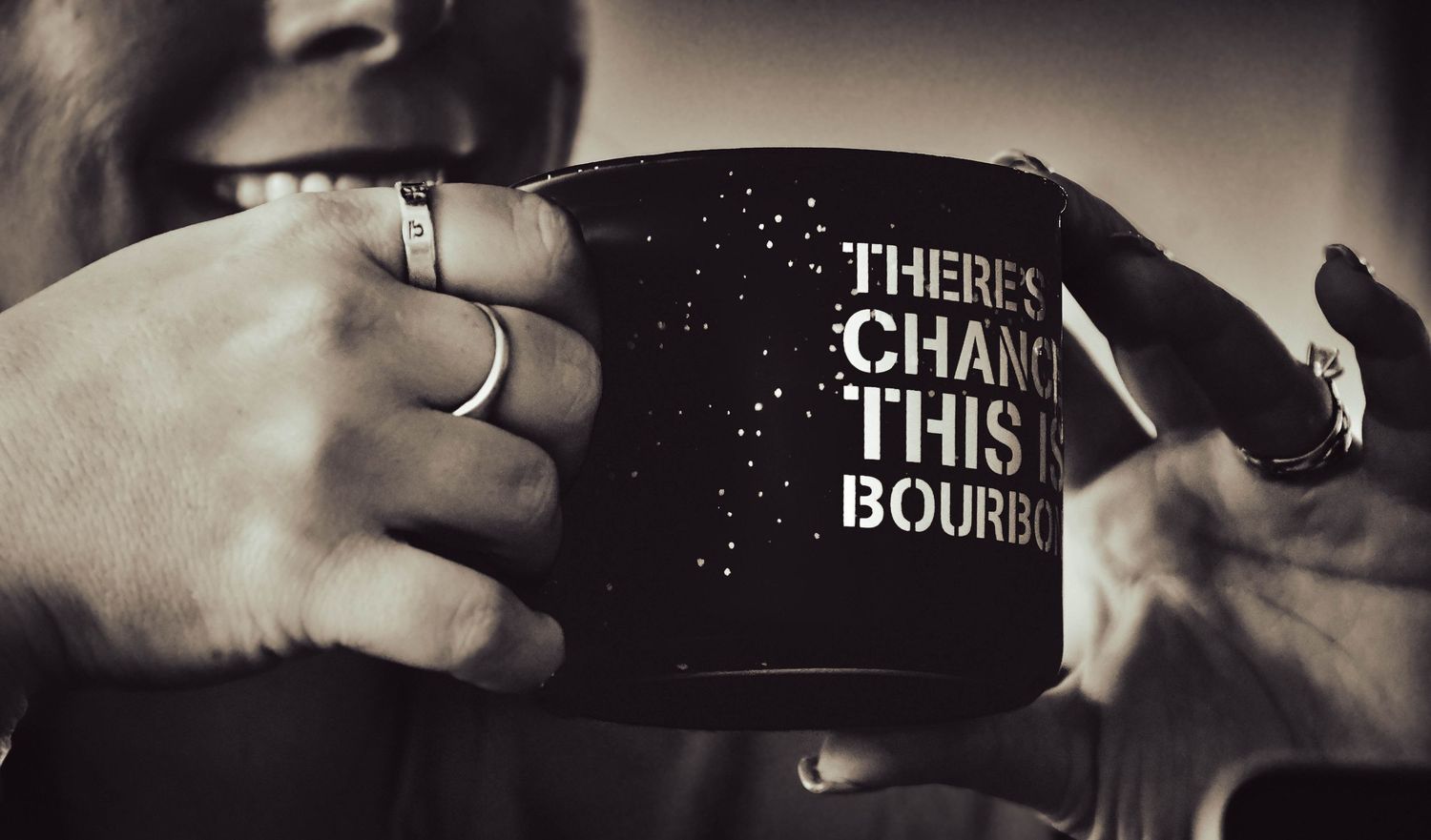 Person holding a black mug reading There's a Chance This is Bourbon in a black and white photo.