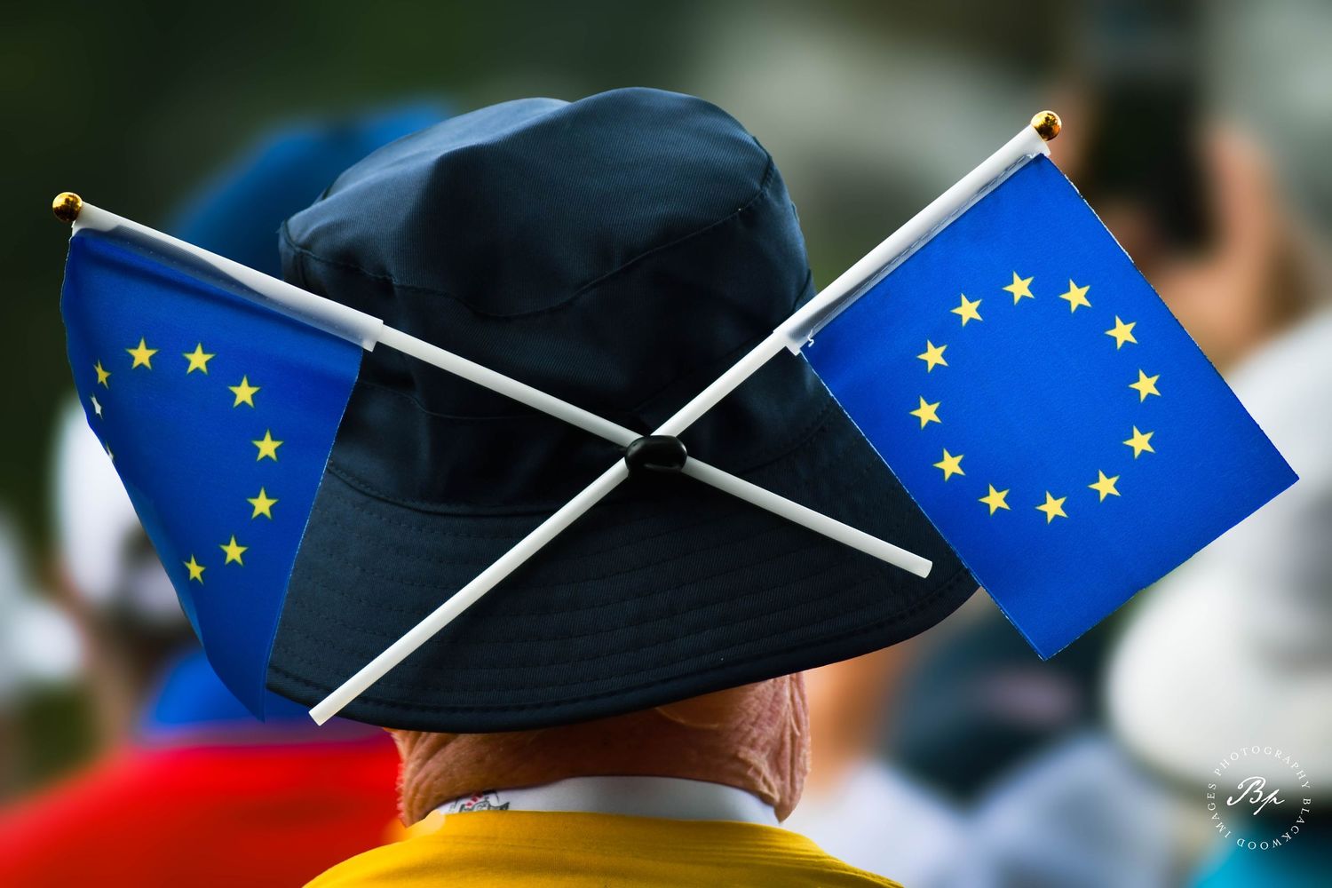 Person wearing a bucket hat adorned with two crossed European Union flags outdoors.
