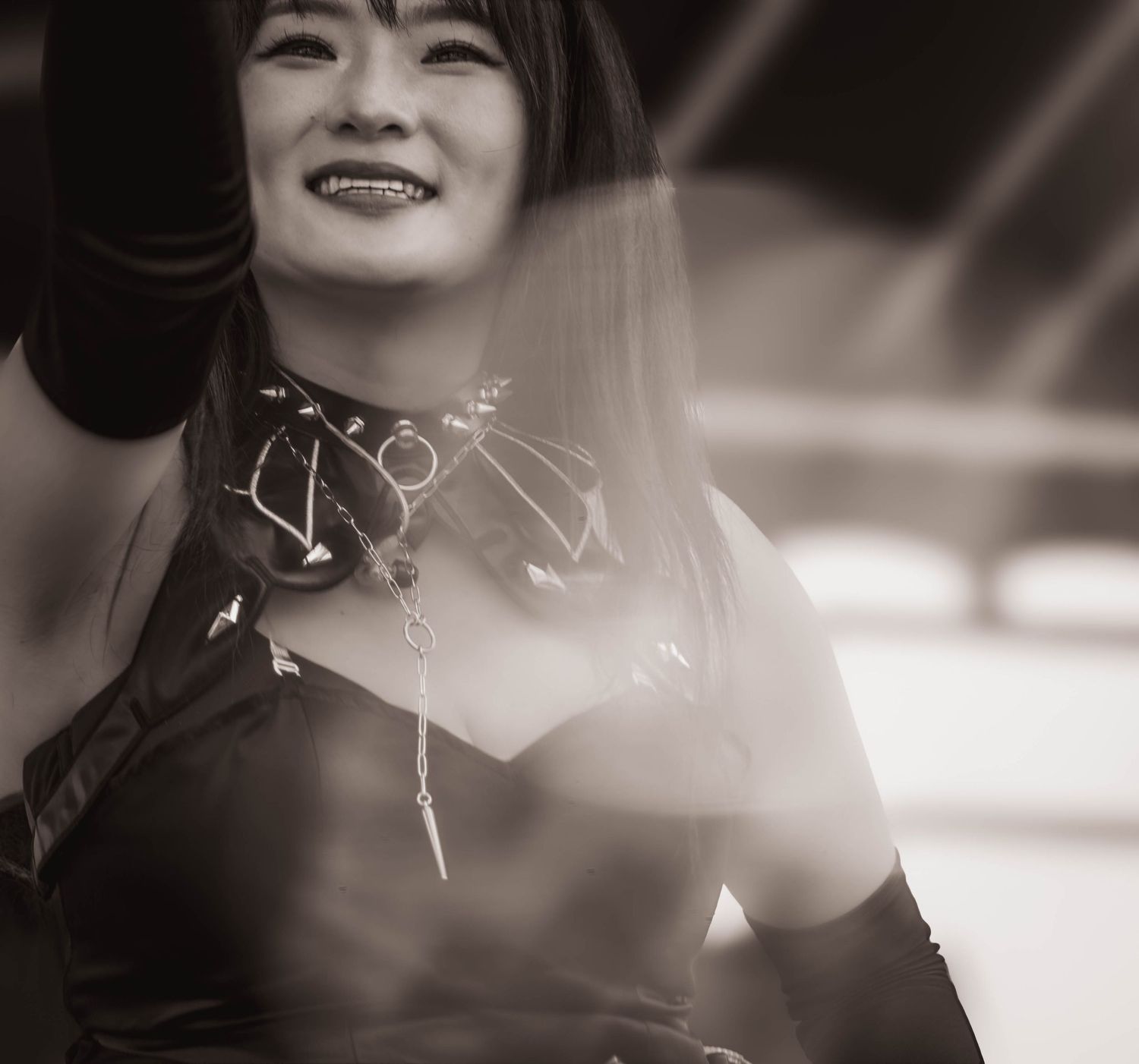 Black and white photo of a smiling young woman in stylish dark outfit with accessories performing on stage.