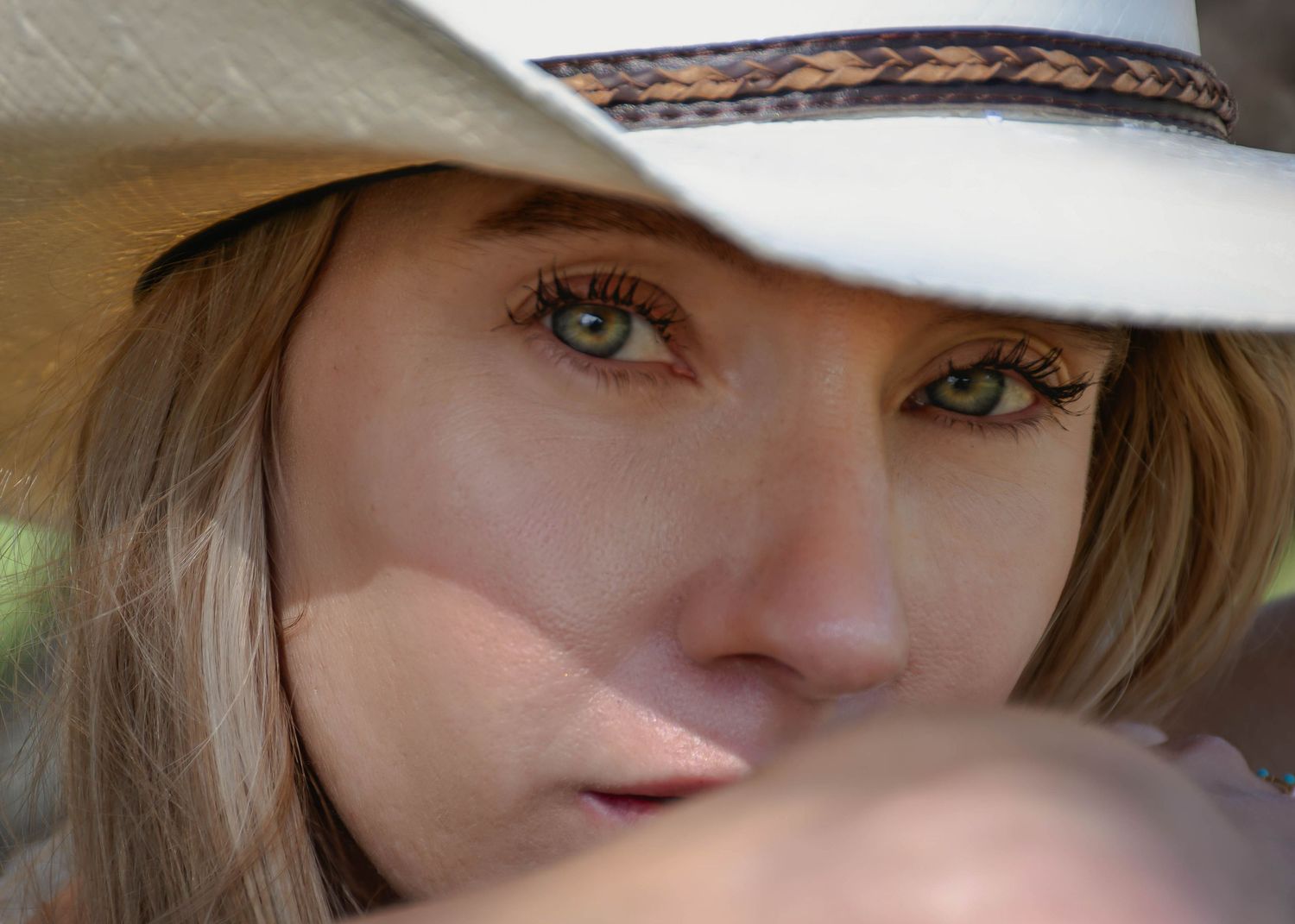 Close-up of woman with green eyes wearing white cowboy hat with braided band looking intensely at camera.