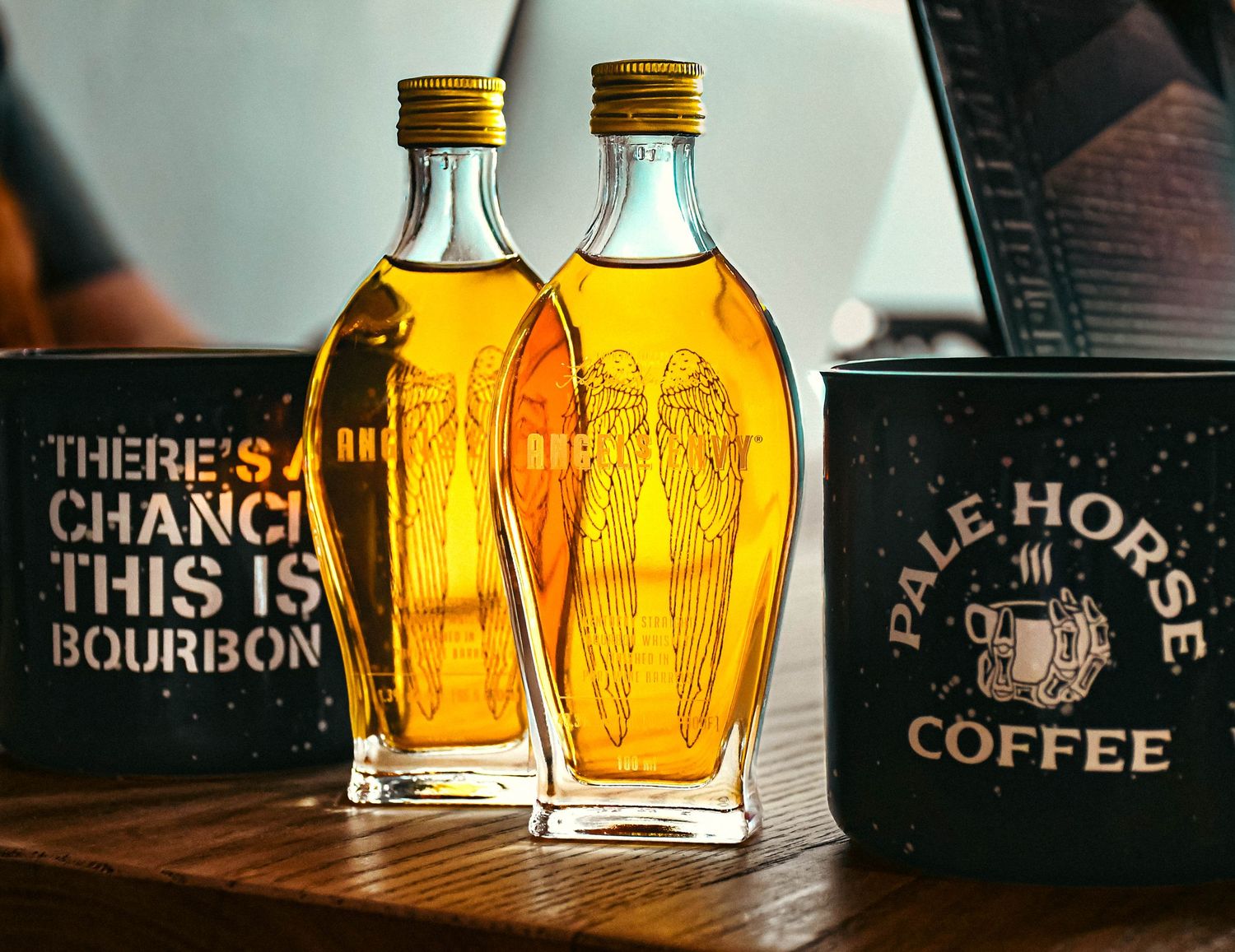 Two decorative bourbon bottles beside a Pale Horse Coffee mug on a wooden table.