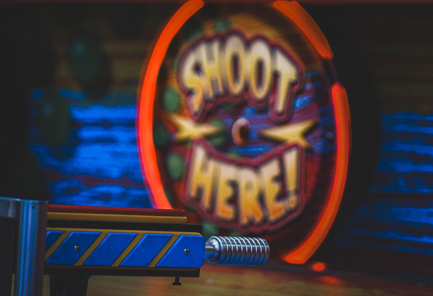 Neon arcade shooting gallery sign reading Shoot Here with a toy gun in the foreground.
