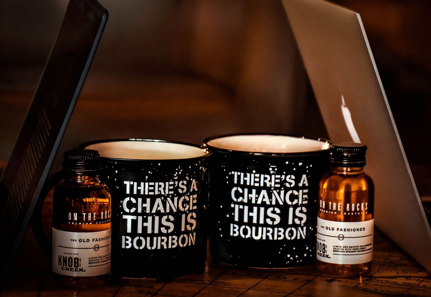 Two black mugs reading There's a Chance This Is Bourbon beside bourbon bottles on table.