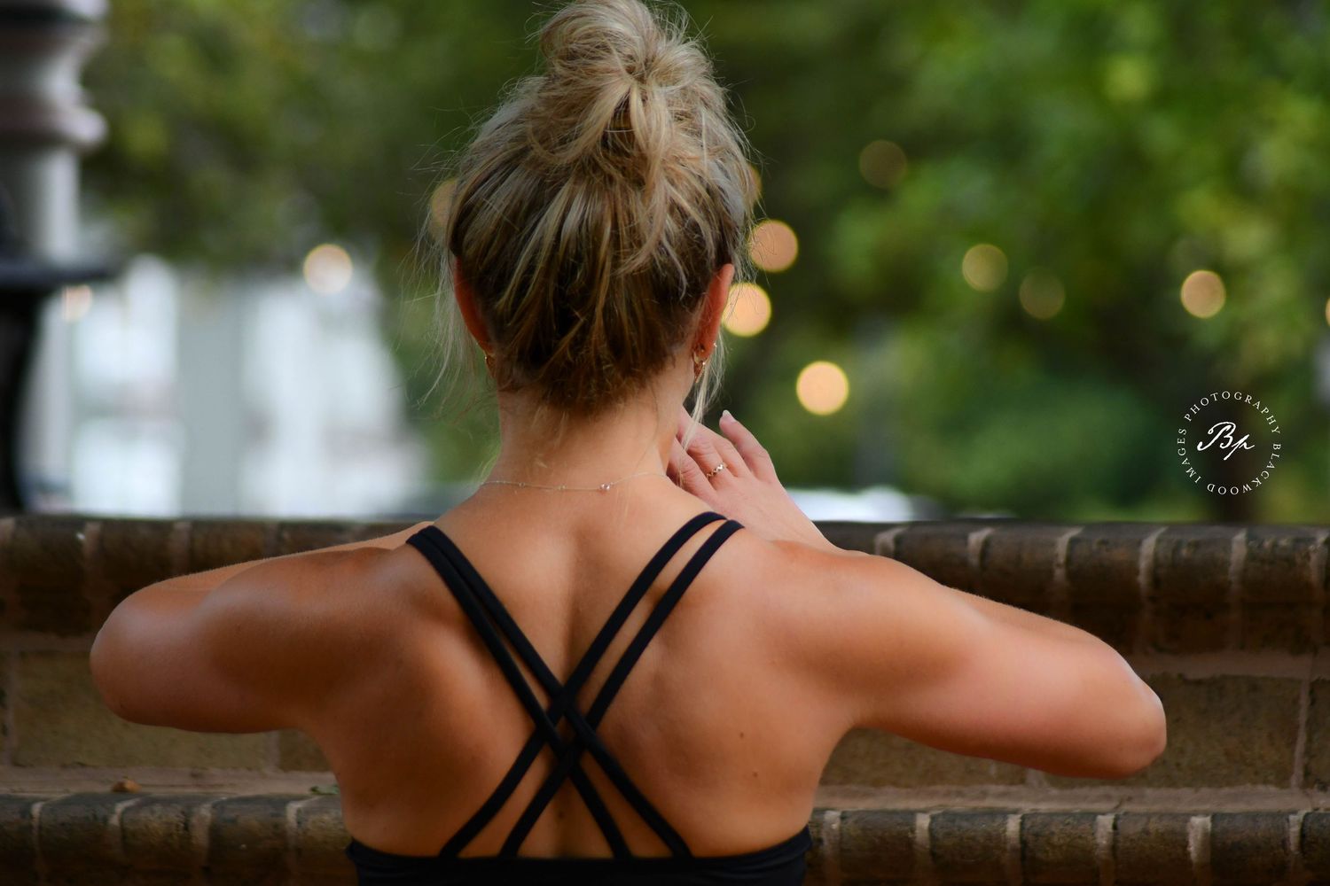Athletic woman in black strappy sports bra touches her neck while sitting outdoors.