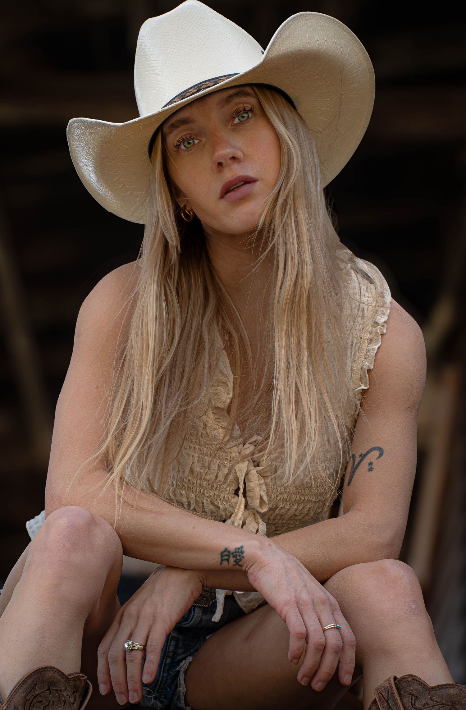Blonde woman in white cowboy hat and tan smocked top poses confidently outdoors.
