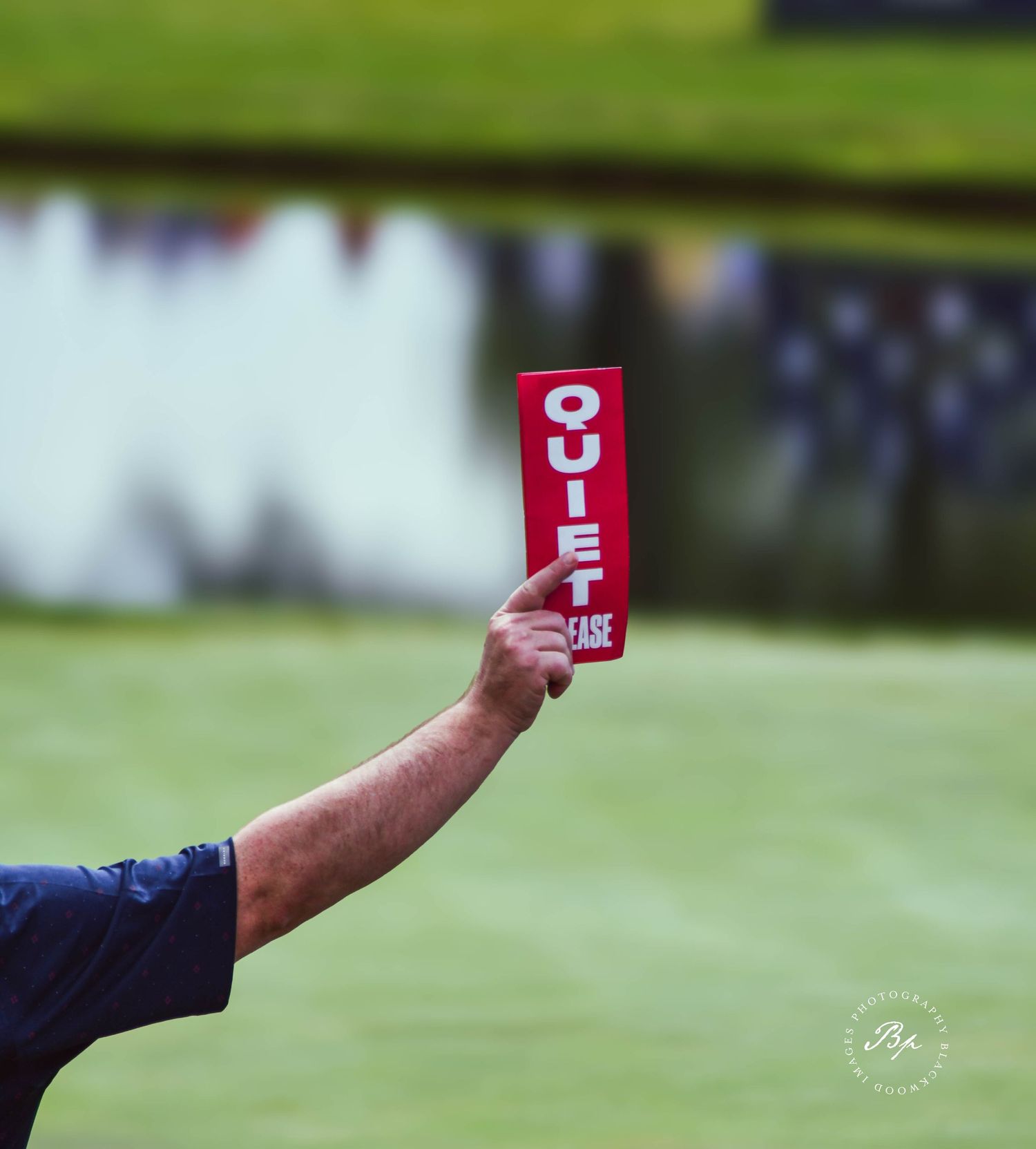 Golf marshal holding a red Quiet Please sign near a green during a tournament.