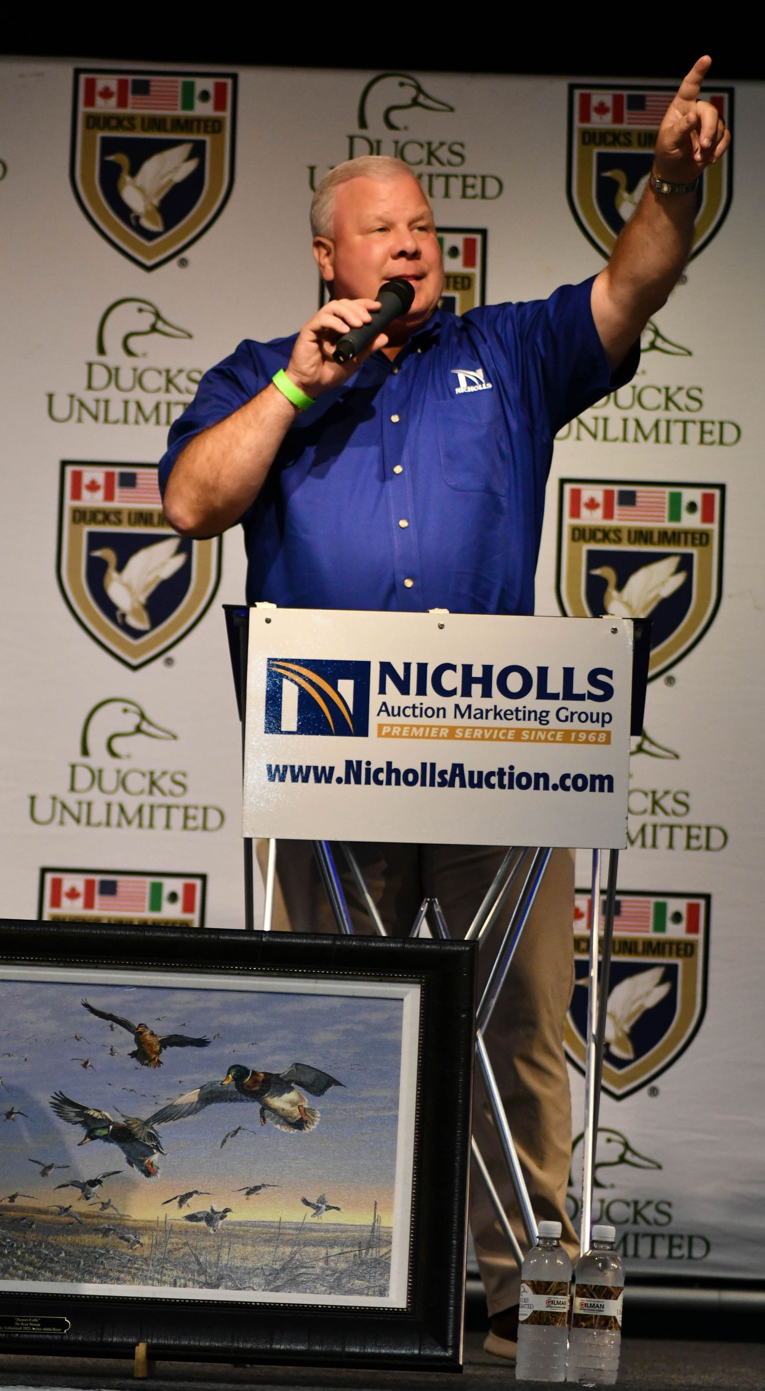 Auctioneer speaking at a Ducks Unlimited charity auction event at a Nicholls podium.