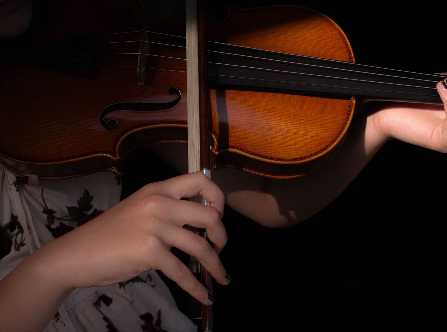 Close-up of a child's hands playing violin with bow, showcasing string instrument technique in dim lighting.