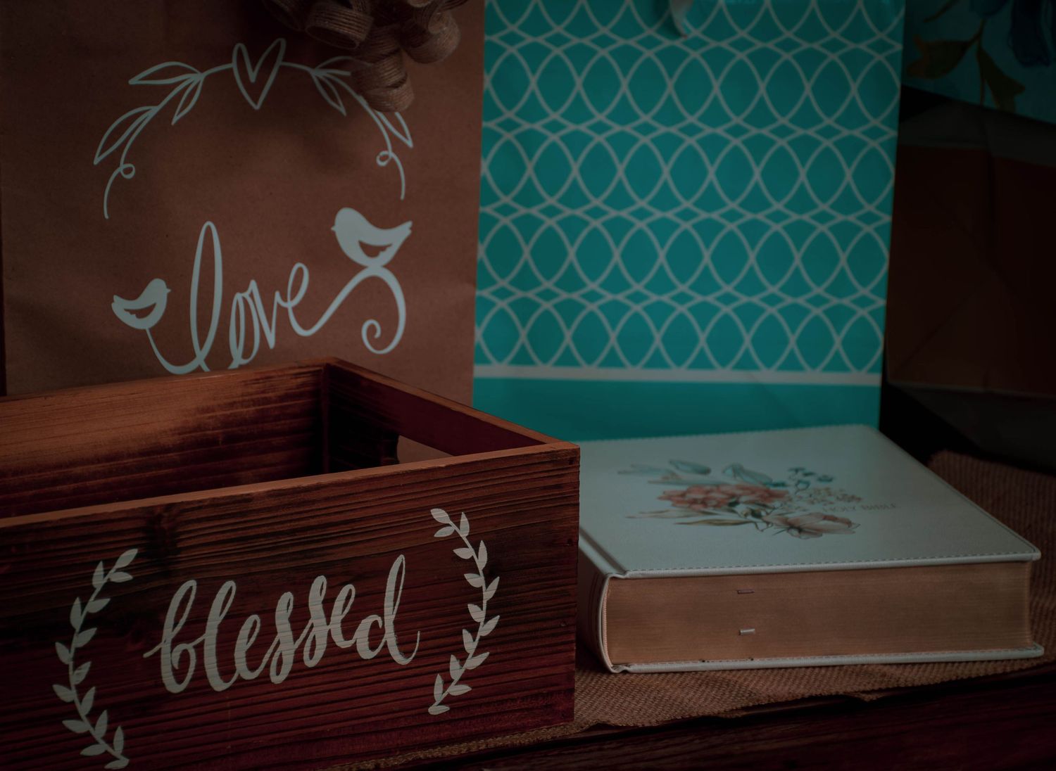 Rustic wooden blessed box beside a book and brown love bag with teal patterned backdrop.
