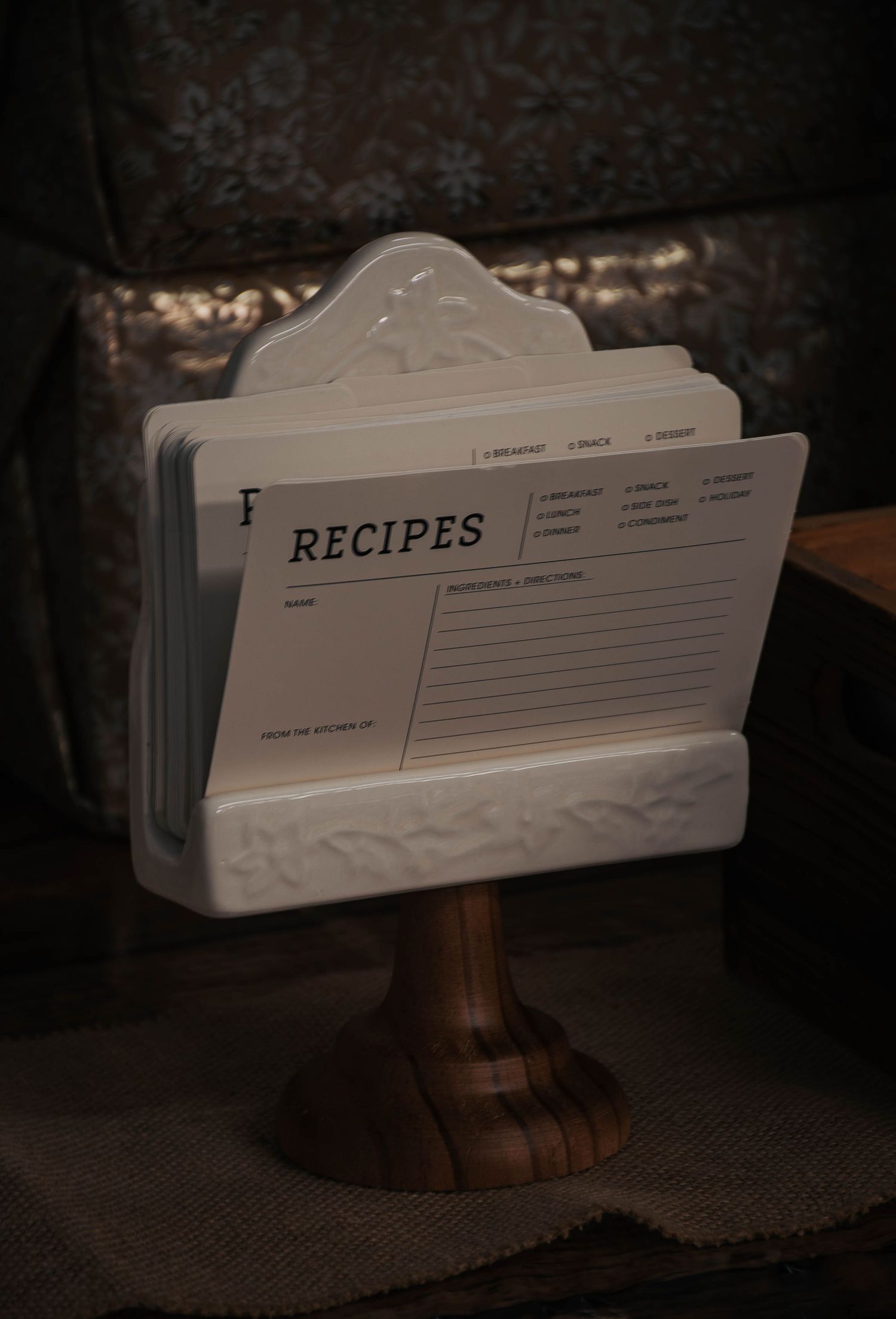 White ceramic recipe card holder on wooden pedestal stand with blank recipe cards, perfect for kitchen organization.
