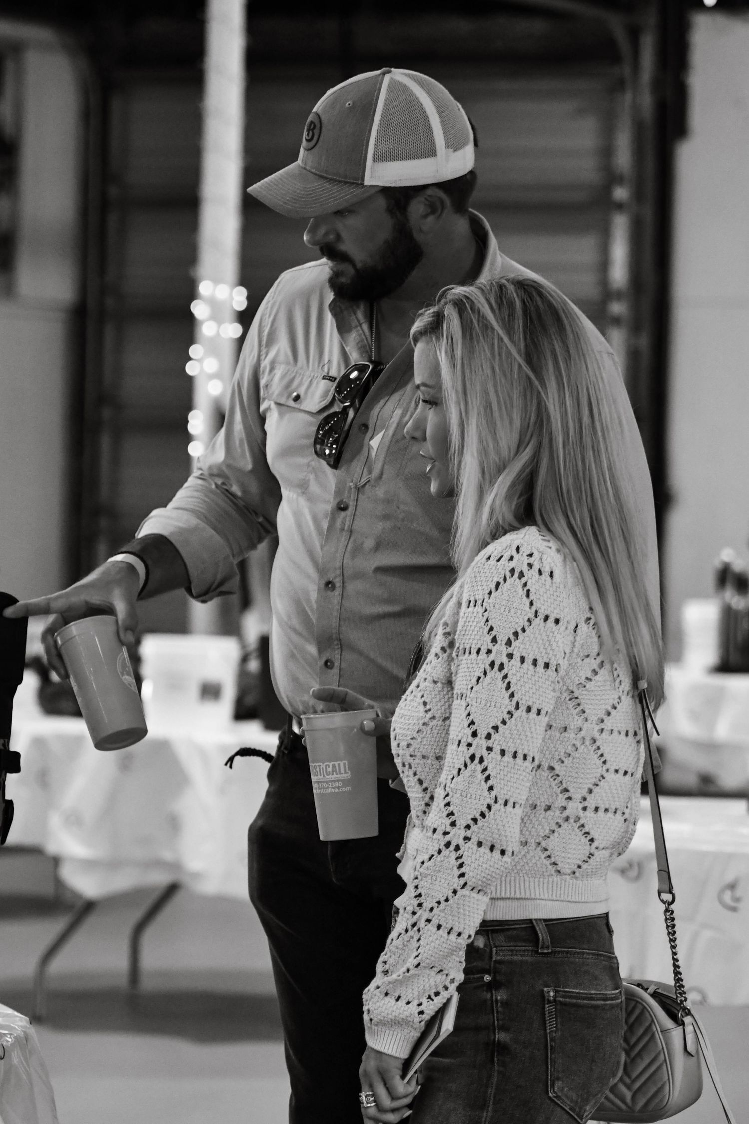 Black and white photo of a man and blonde woman looking at drinks at an indoor event.