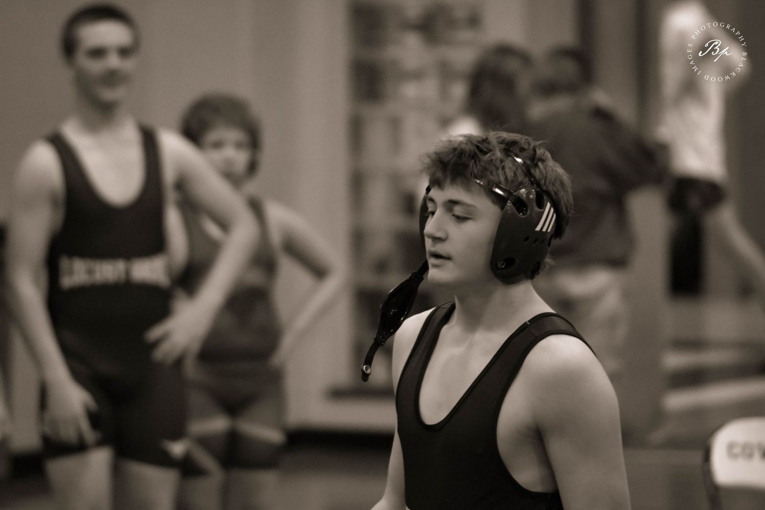 Black and white photo of a young wrestler in headgear standing on a wrestling mat.