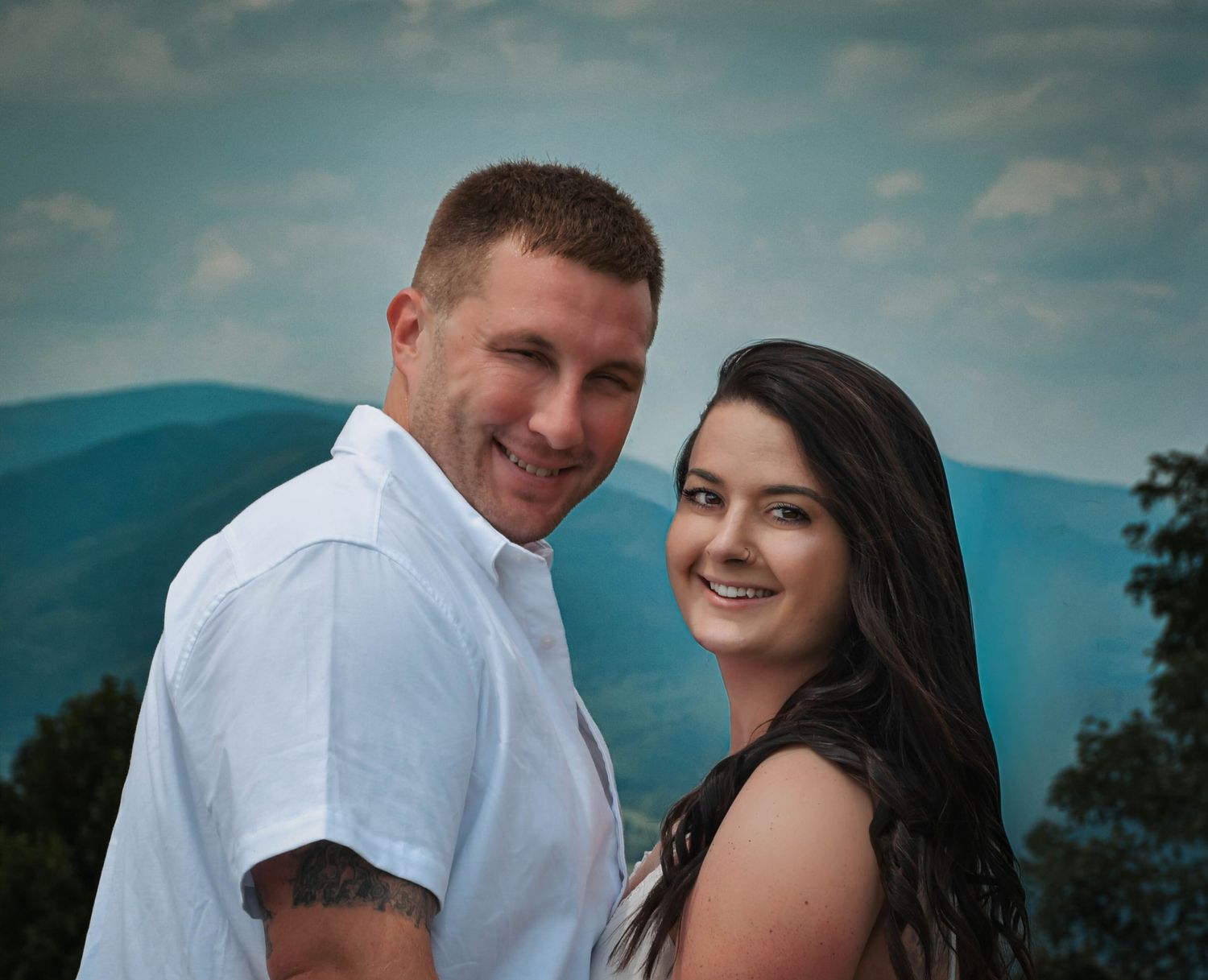 Smiling couple posing outdoors with scenic blue mountain landscape backdrop in a portrait photo.