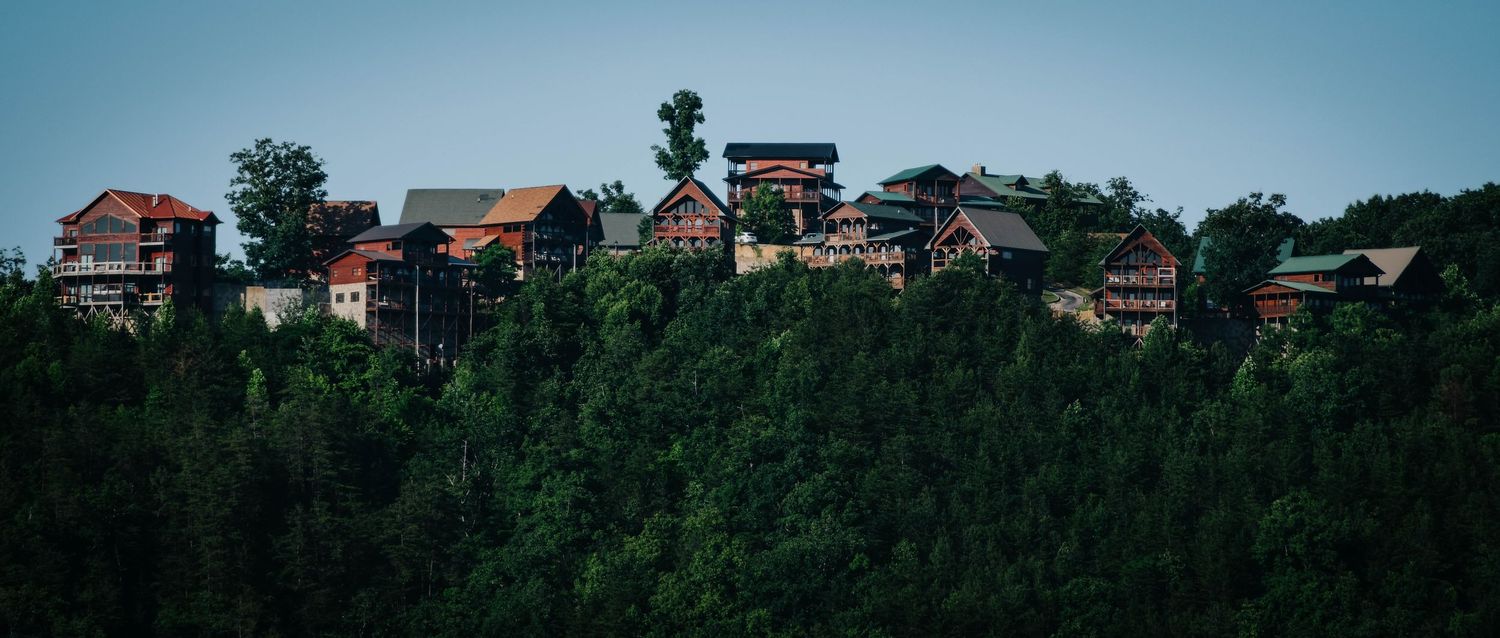 Hilltop Skii village with rustic houses nestled among dense green trees against a clear blue sky.