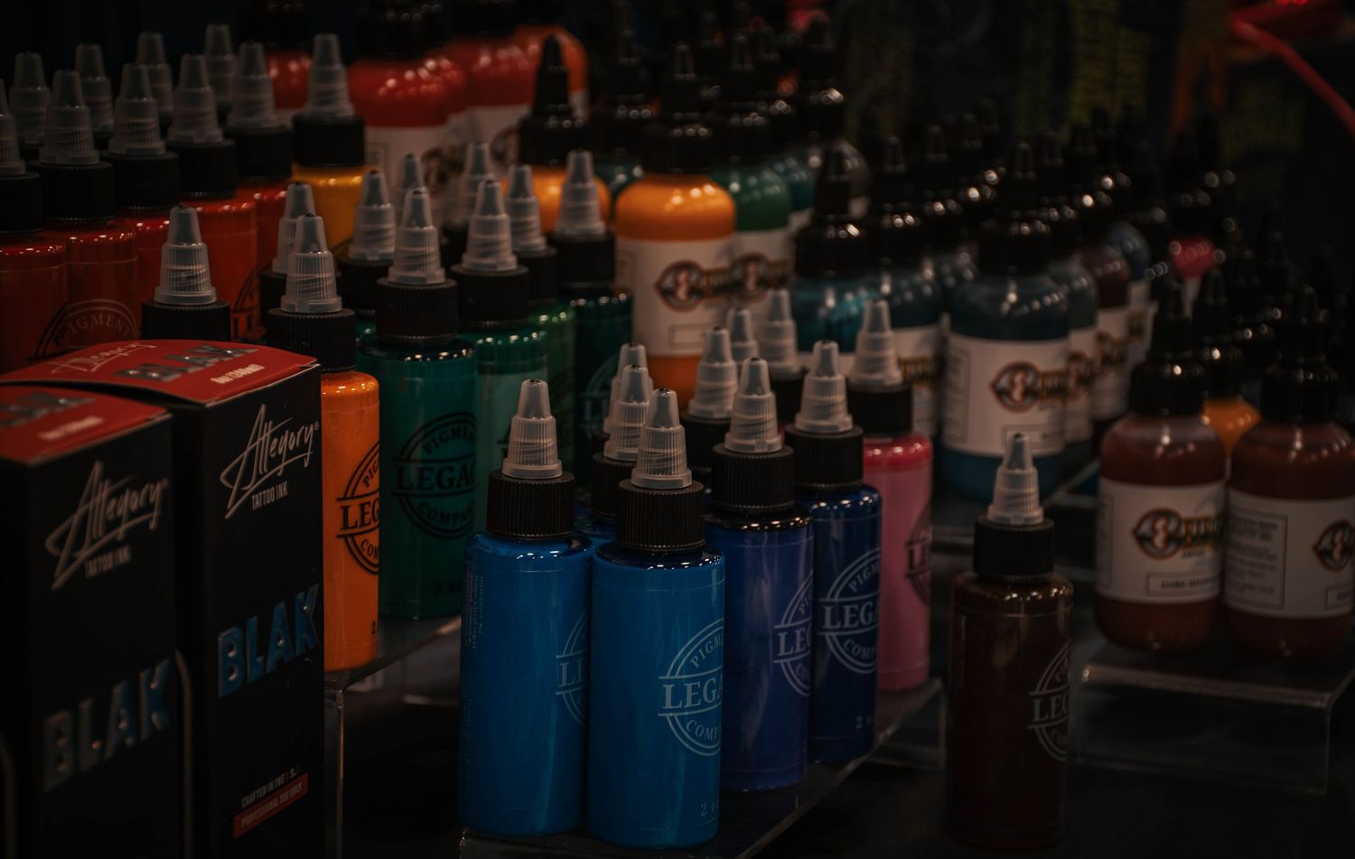 Colorful tattoo ink bottles displayed on a table, featuring brands like Bloodline and Alla Prima at a tattoo convention.
