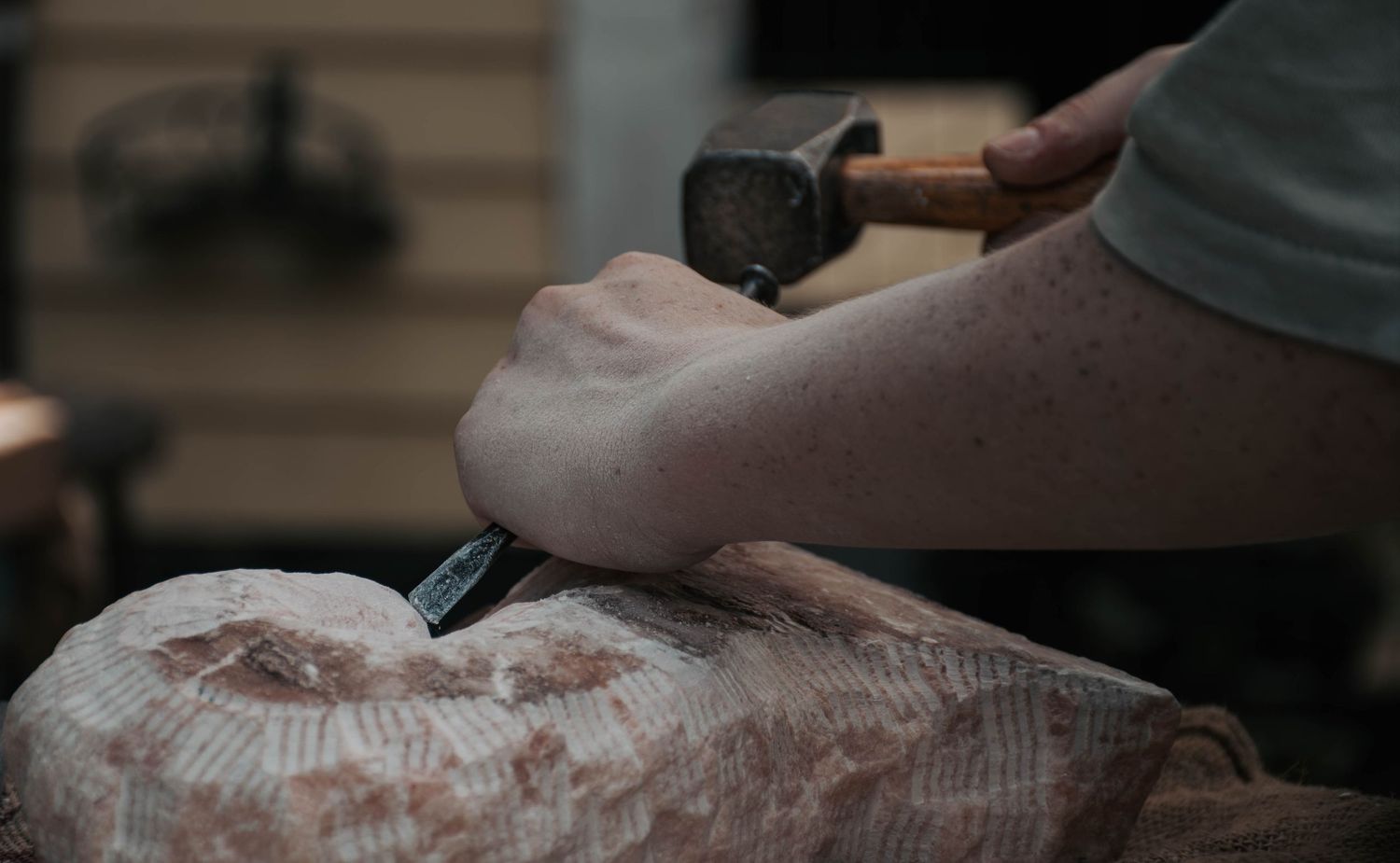 A craftsman uses a hammer and chisel to carve a stone sculpture in a workshop.