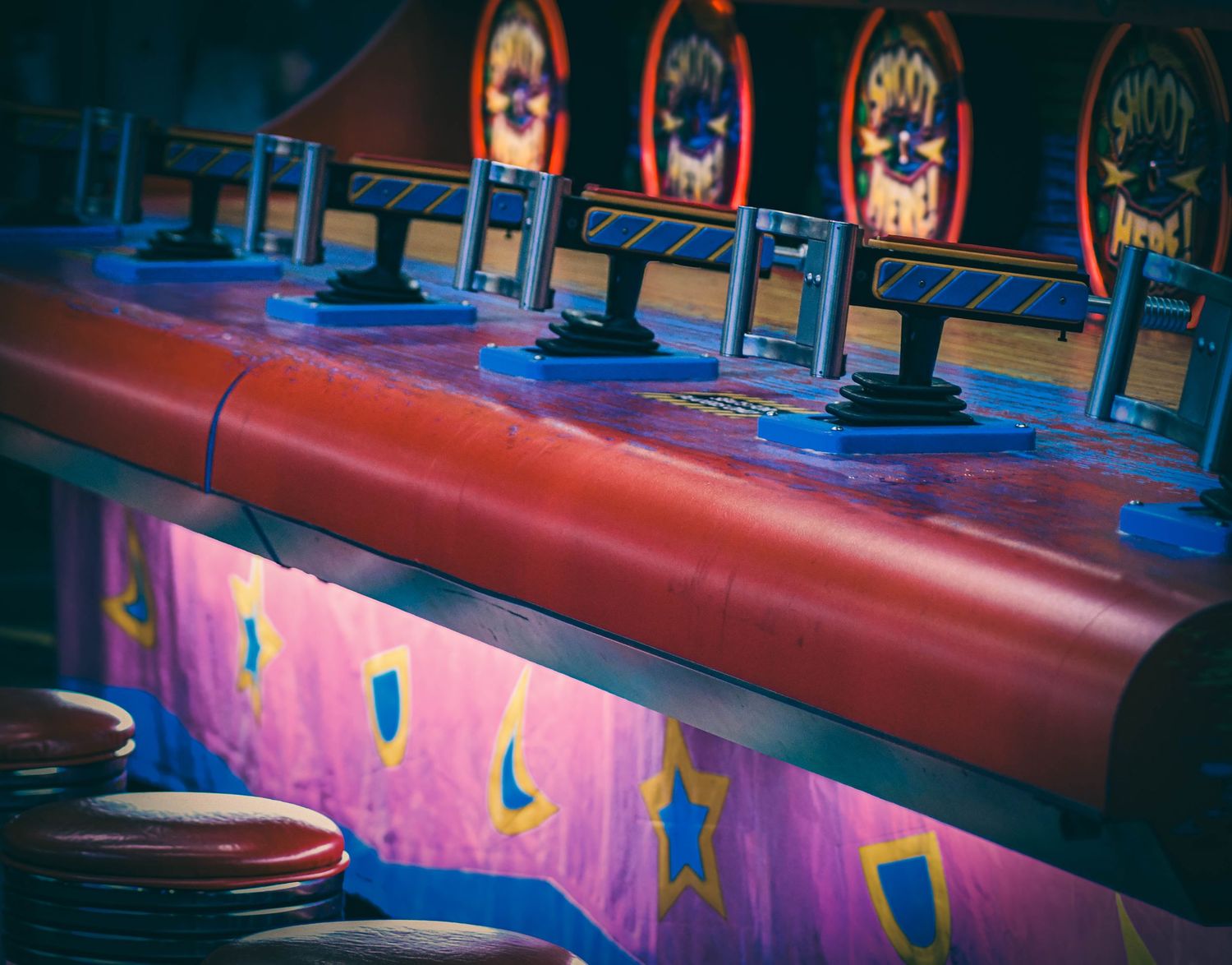Colorful carnival skee-ball game lanes with red rails, glowing purple panels, and star decorations at an amusement arcade.