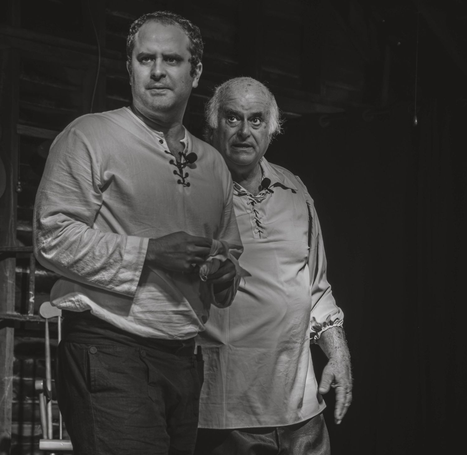 Two men posing together in black and white portrait photo, wearing casual tops in a dimly lit setting.