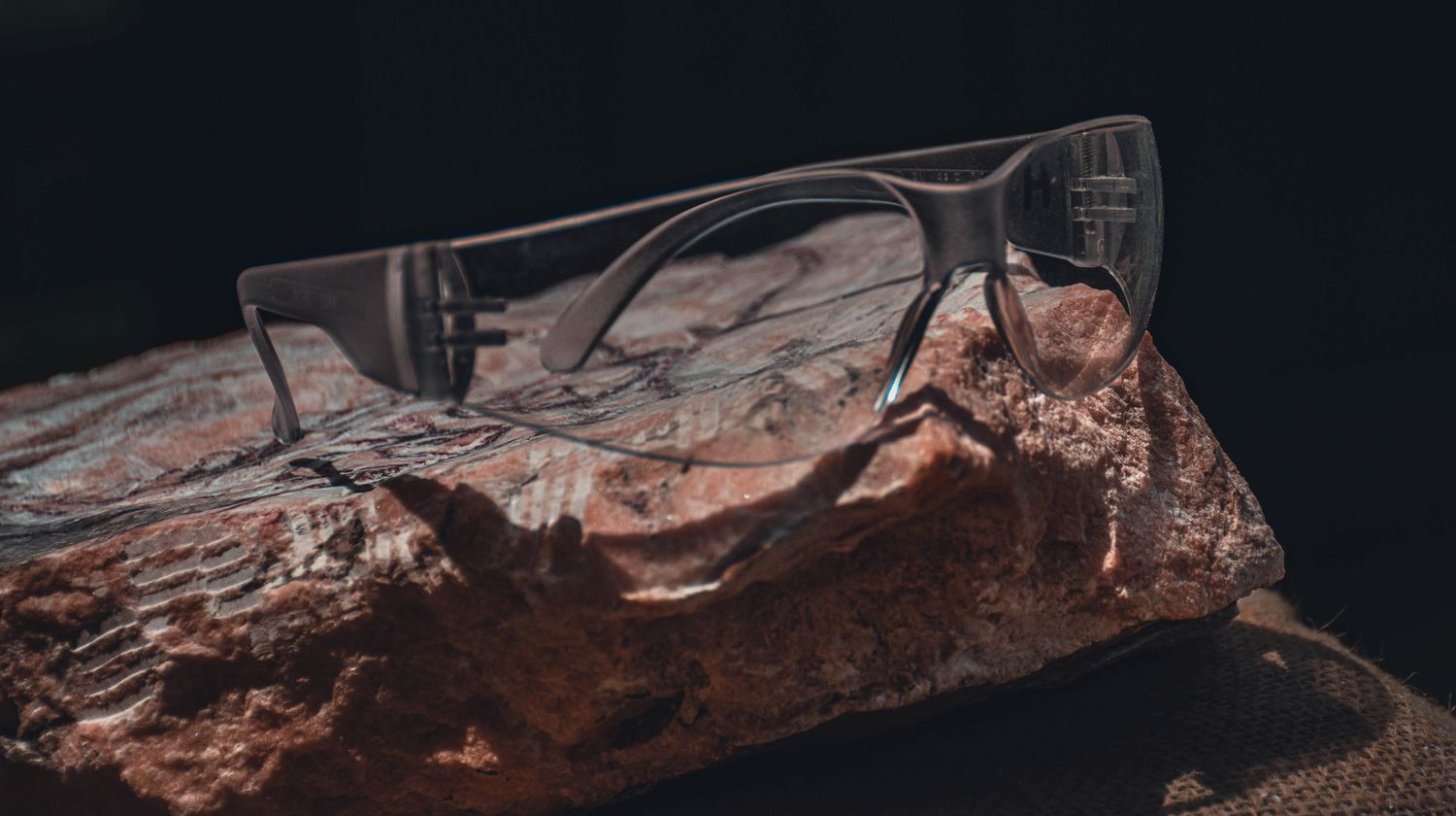 Clear rimless glasses resting on a rustic wooden surface against a dark background.
