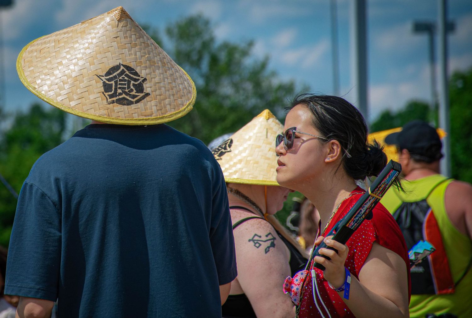 Two people wearing traditional Asian conical hats at an outdoor festival on a sunny day.