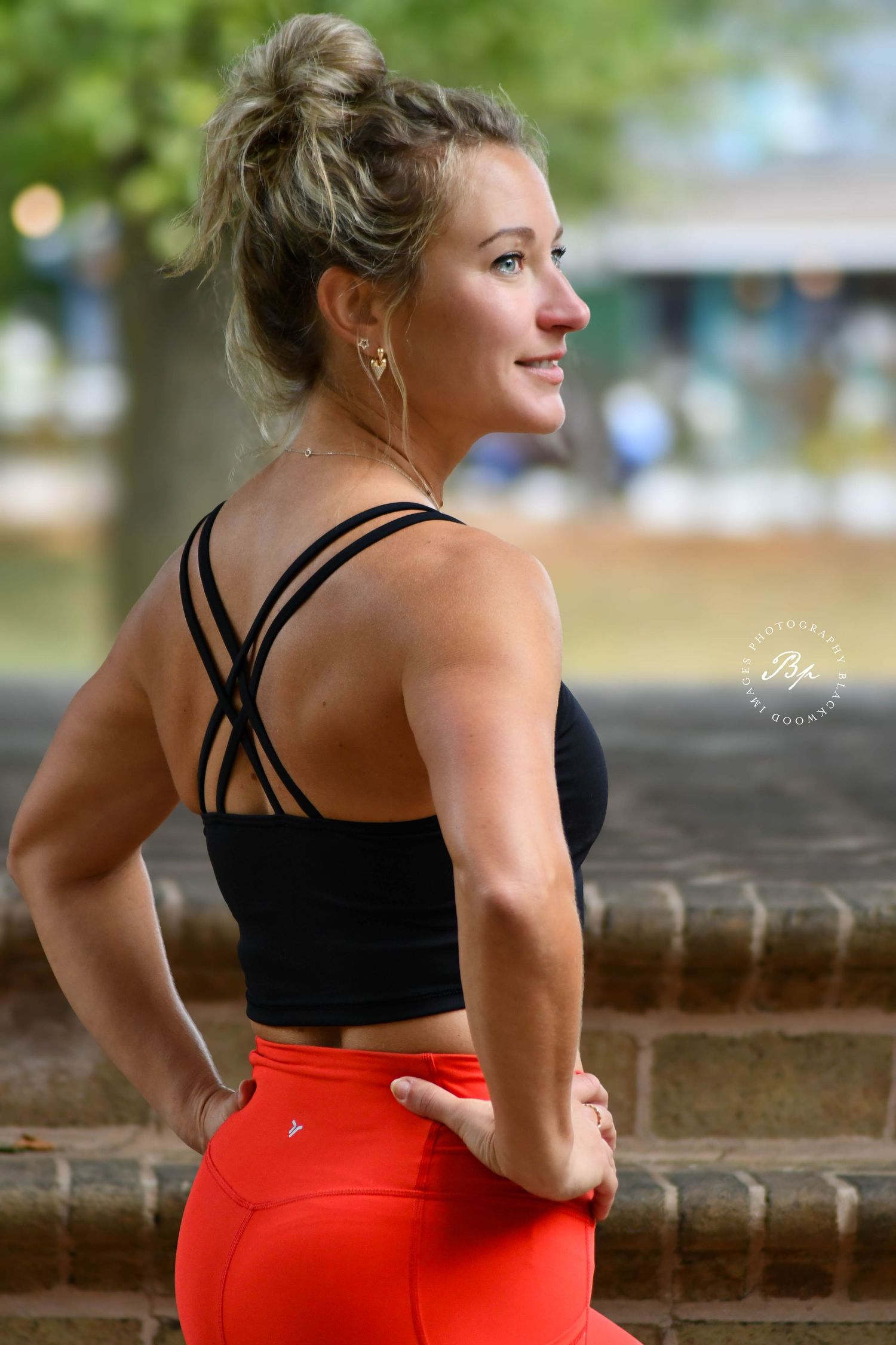 Athletic woman in black strappy sports bra and red leggings smiles in outdoor setting.