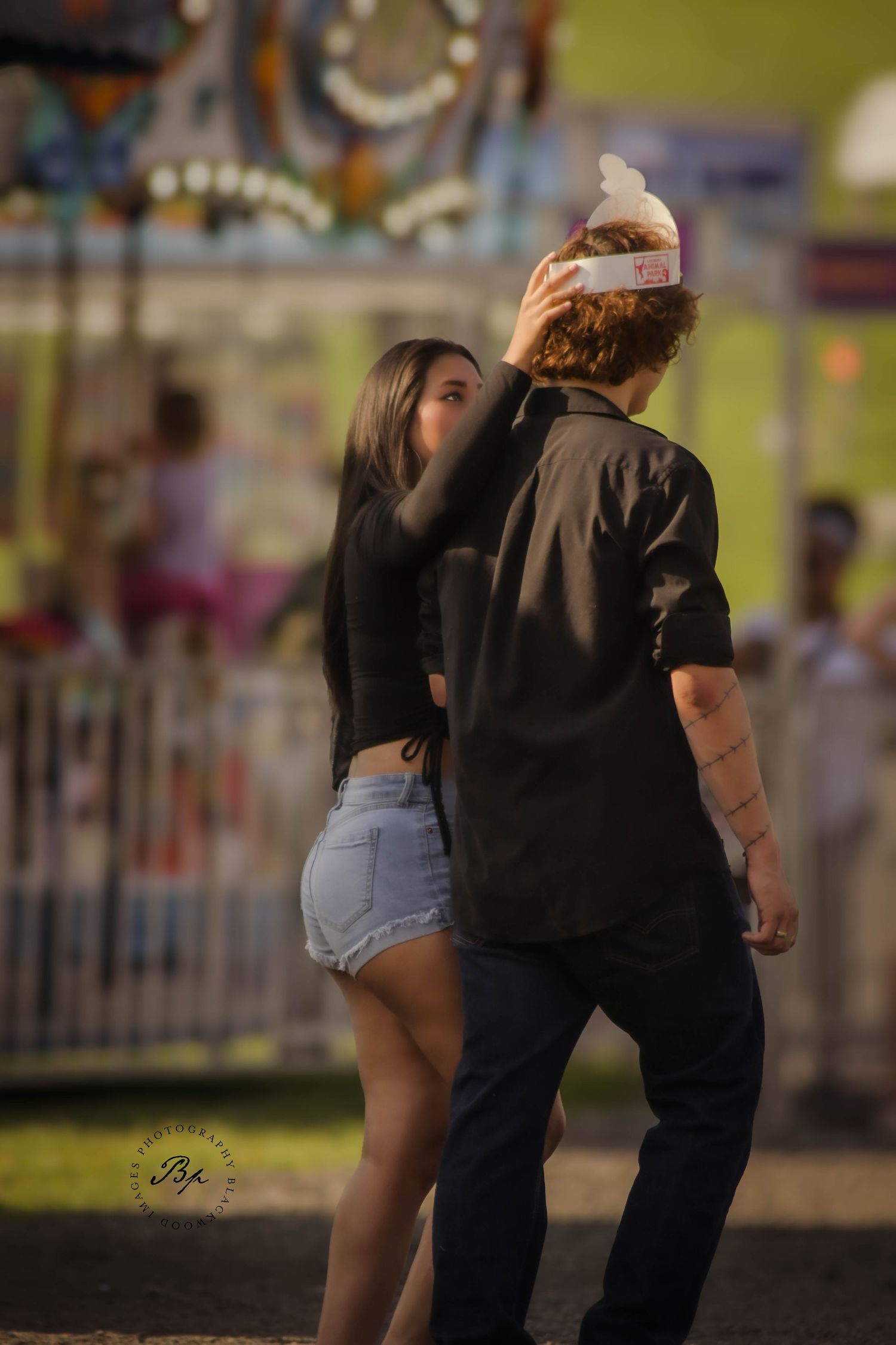 Young couple dancing together at colorful outdoor carnival fairground at dusk.