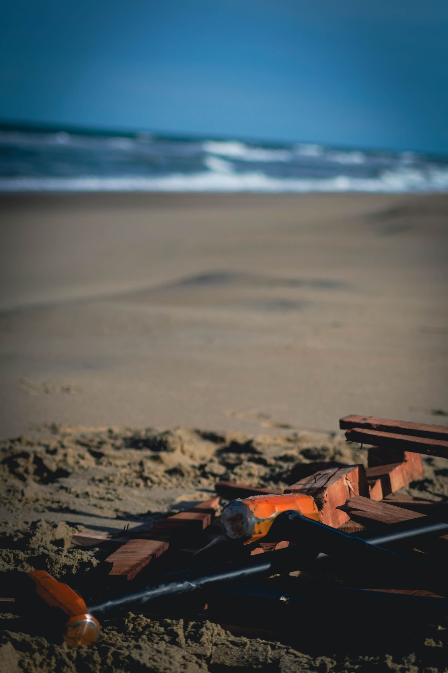 Broken wooden crate with orange pieces scattered on a sandy beach under a blue sky.