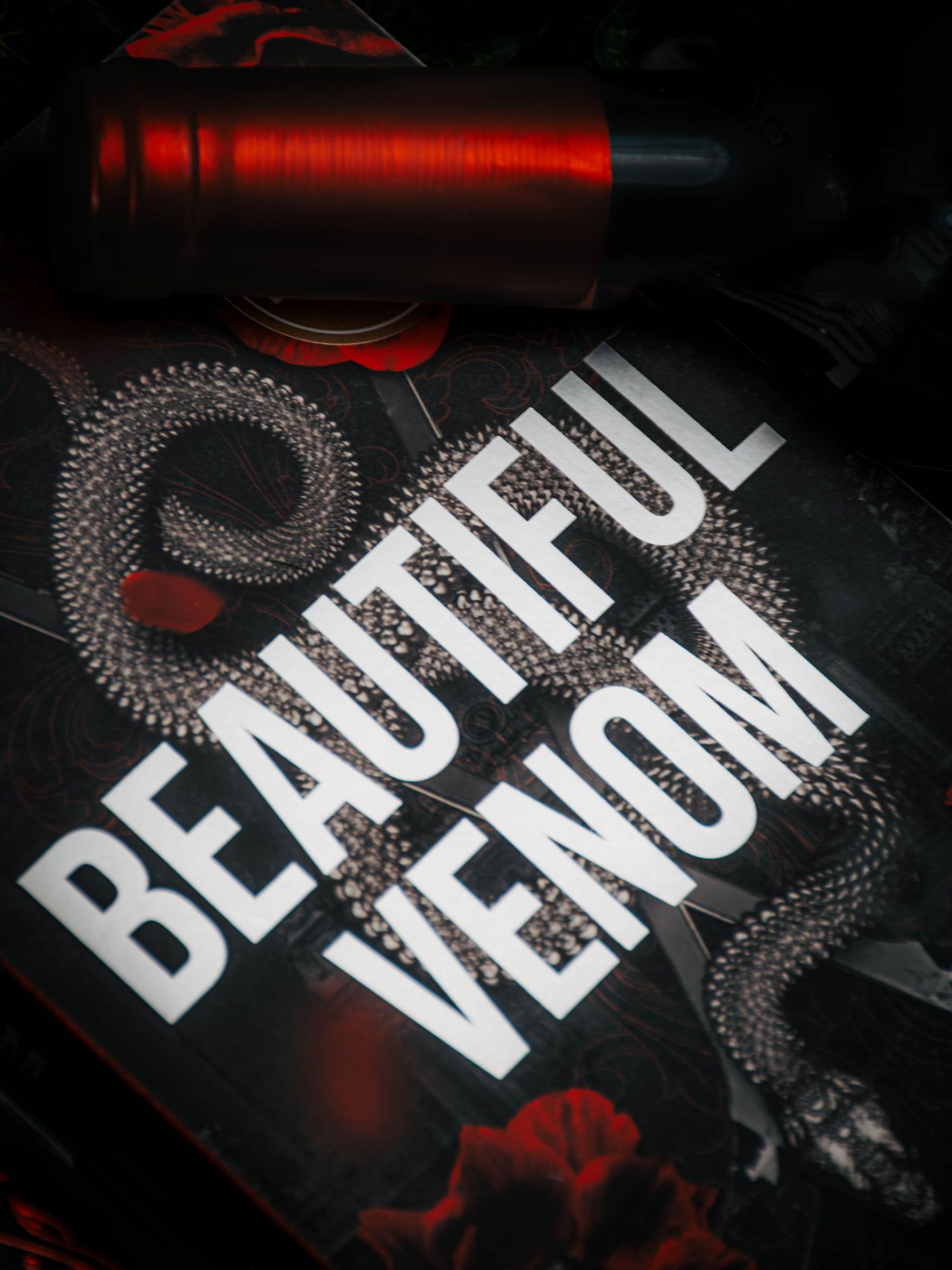 A red tattoo machine beside a dark graphic print reading Beautiful Venom with a snake design.