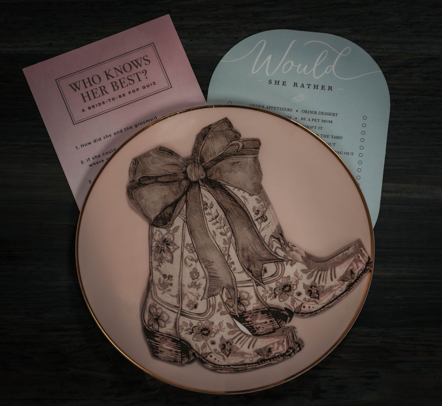 Decorative plate with cowboy boots design beside Who Knows Her Best and Would She Rather bridal shower game cards.