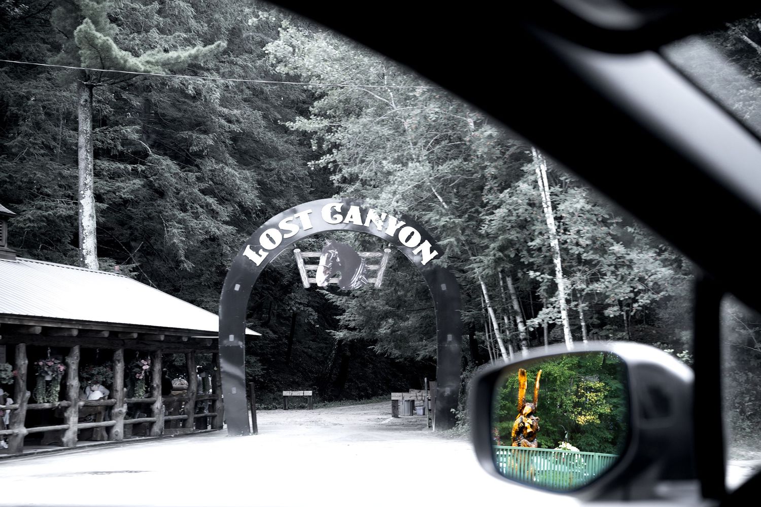 View from a car of Lost Canyon entrance gate surrounded by dense evergreen forest trees.