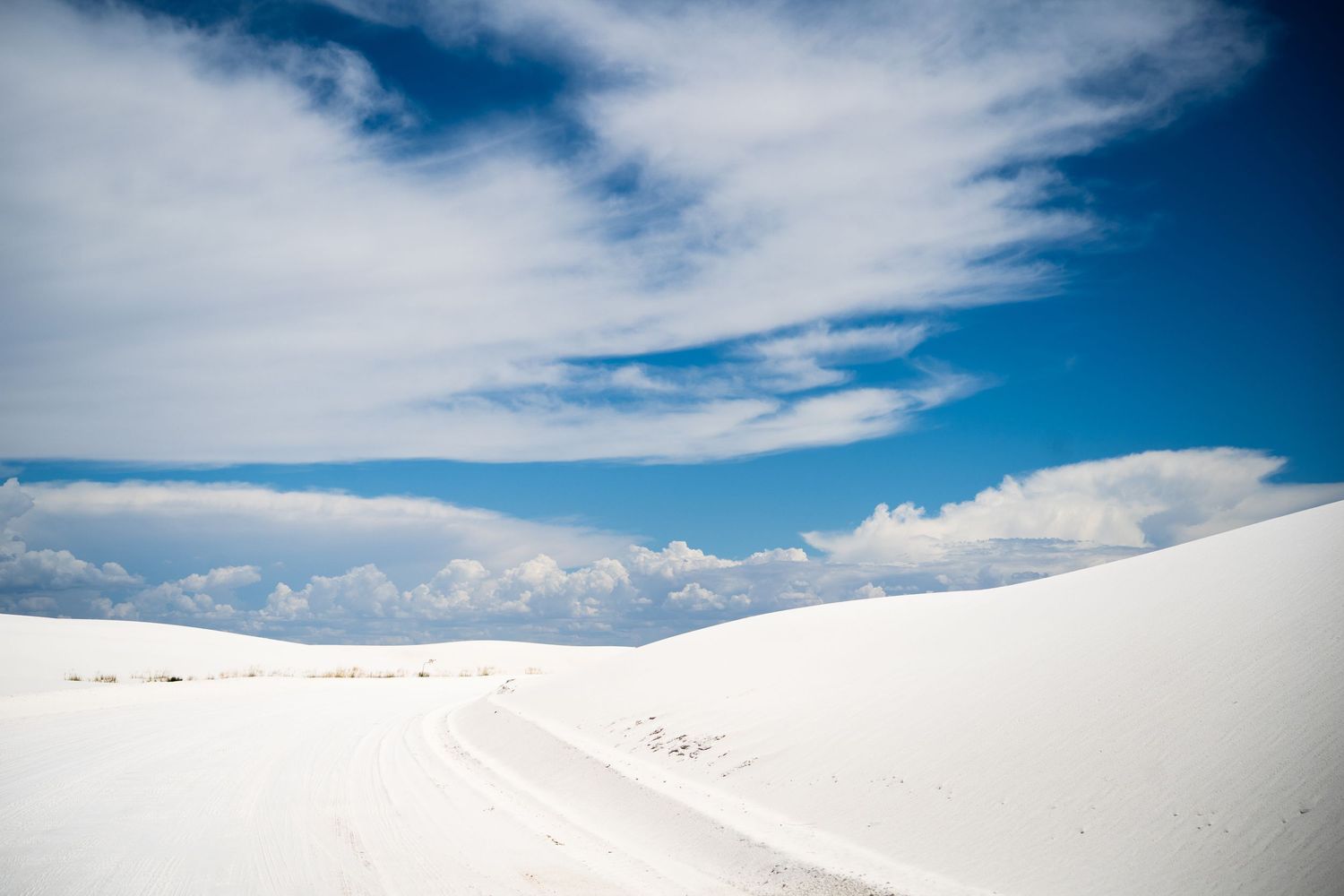 White sand dunes stretch under a vivid blue sky with wispy clouds at White Sands National Park, New Mexico.