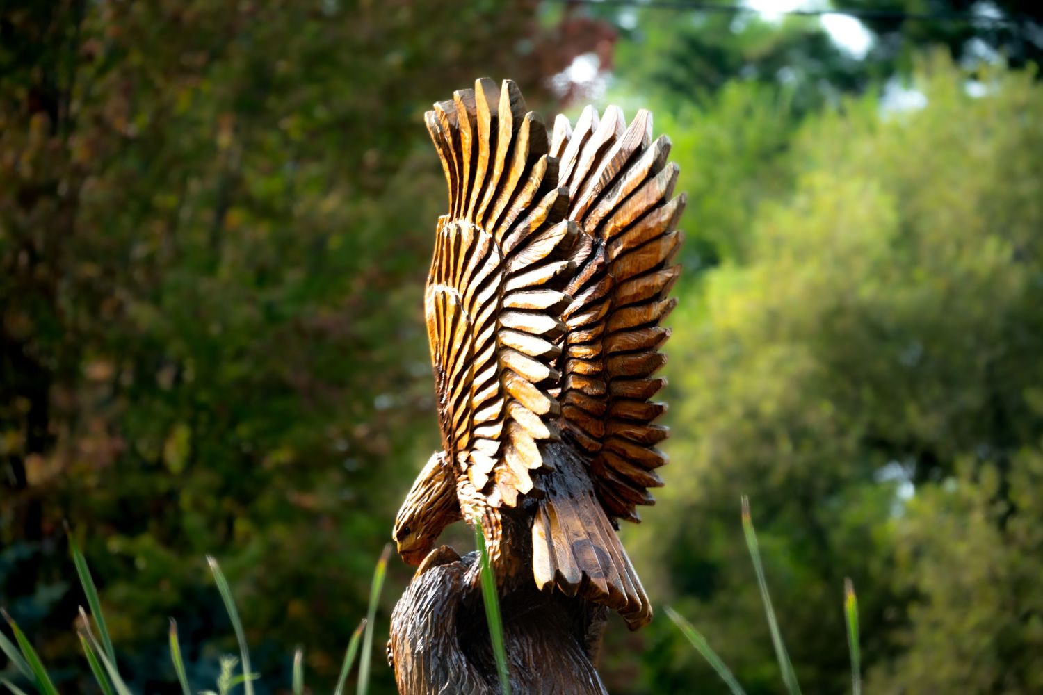 Detailed wooden eagle sculpture with outstretched wings perched on a stump, set against a lush green forest background.